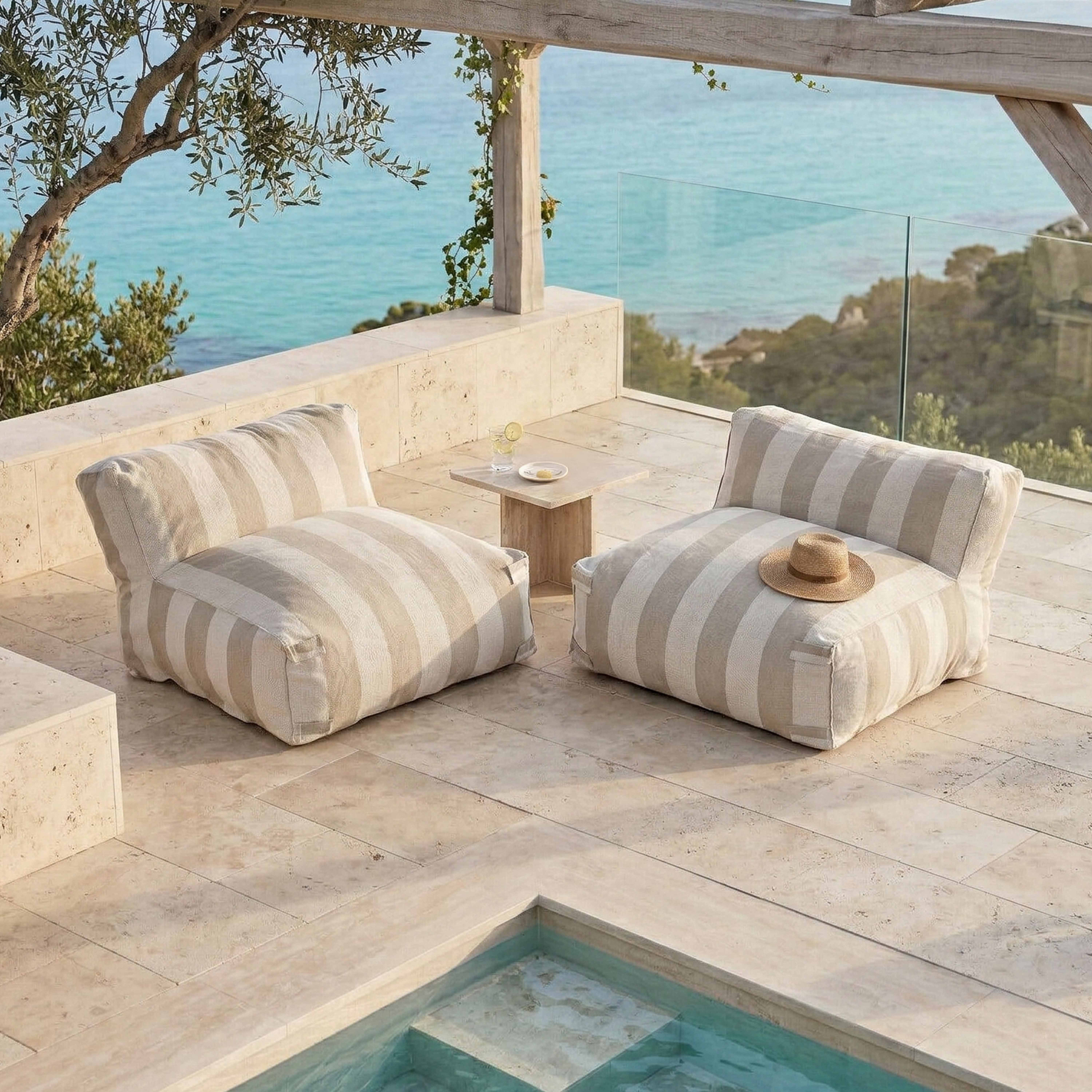 Zwei gestreifte Loungesessel auf einer Terrasse mit Blick aufs Meer. Ein Hut liegt auf einem Sessel.