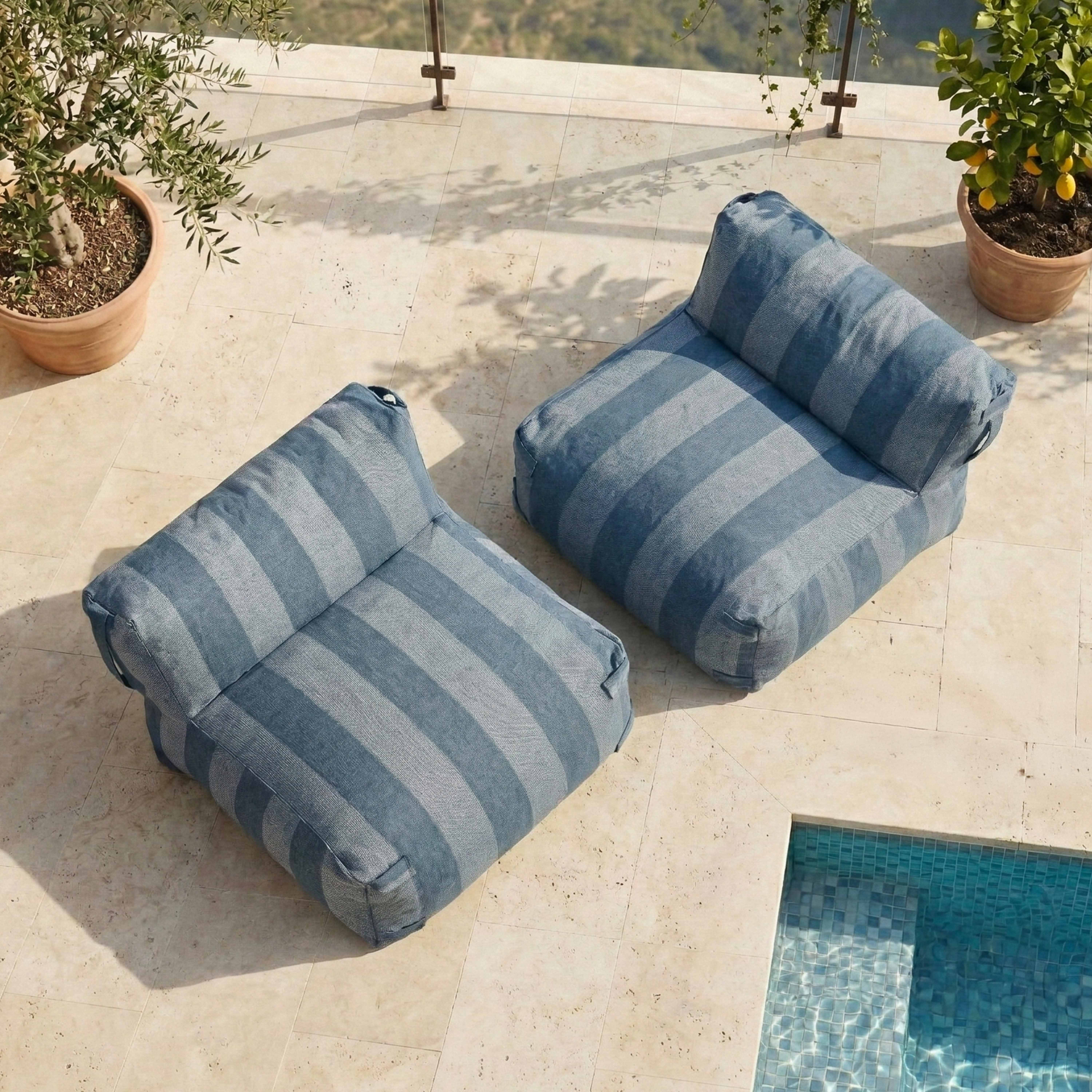 Zwei gestreifte Poufs liegen auf einer beigefarbenen Terrasse neben einem Pool.