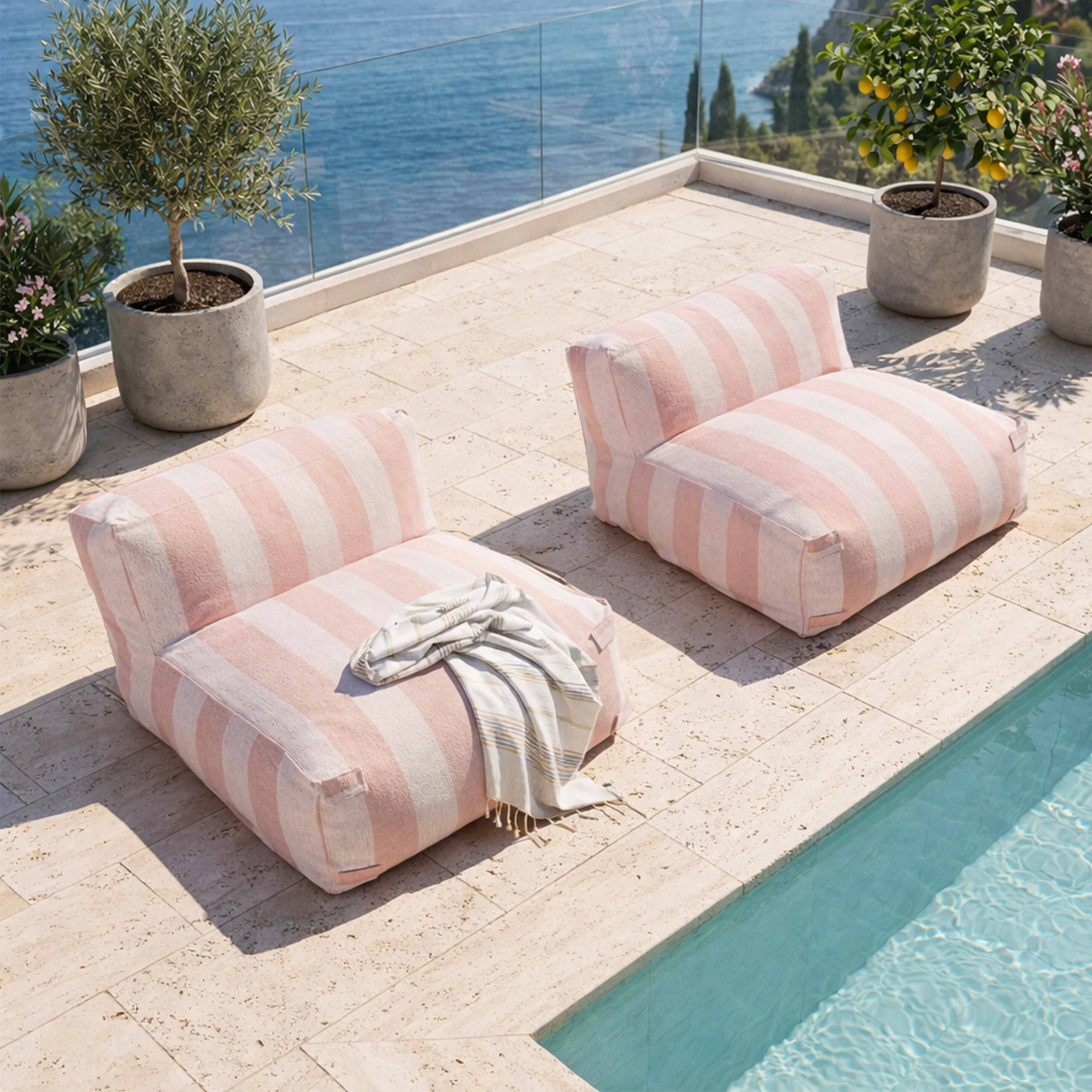 Zwei rosafarbene gestreifte Loungesessel auf einer Terrasse am Meer.