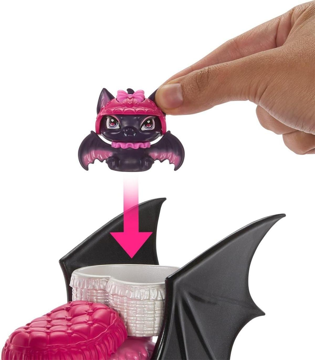 Una mano sostiene un pequeño murciélago de juguete negro con sombrero rosa sobre una cama.