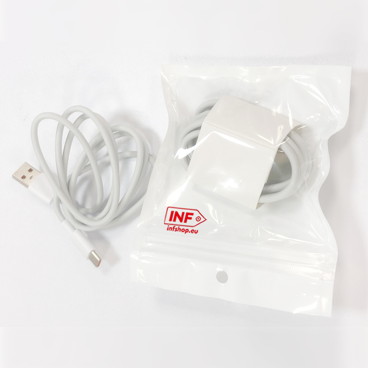 Ein weißes USB-C-Ladekabel liegt links, daneben ein Netzteil in einer Plastiktüte.