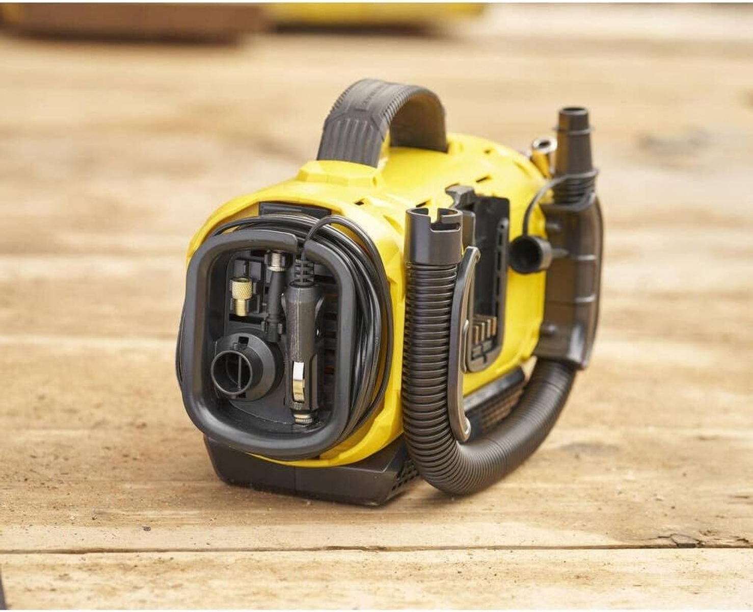 Żółty kompresor powietrza z czarnym wężem i uchwytem na drewnianej powierzchni.