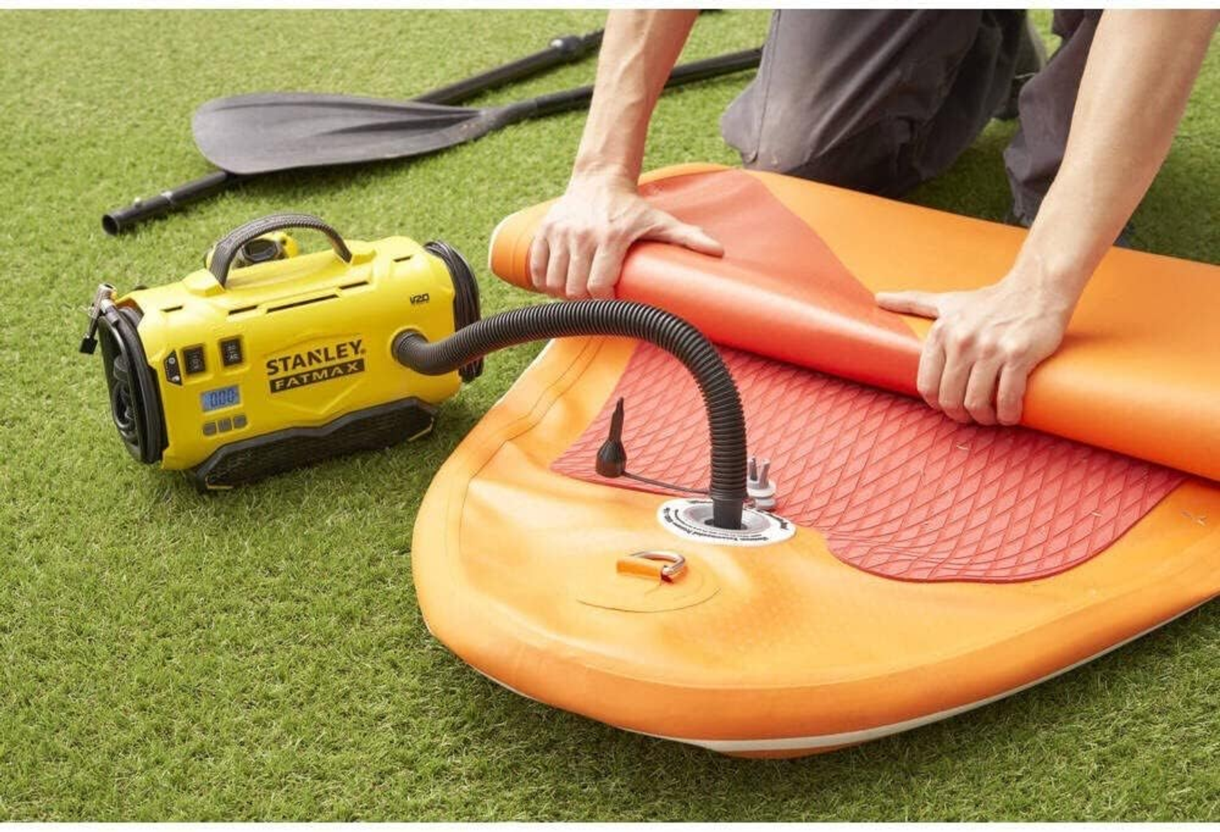 Żółta pompa Stanley podłączona do pomarańczowej deski SUP na trawie.