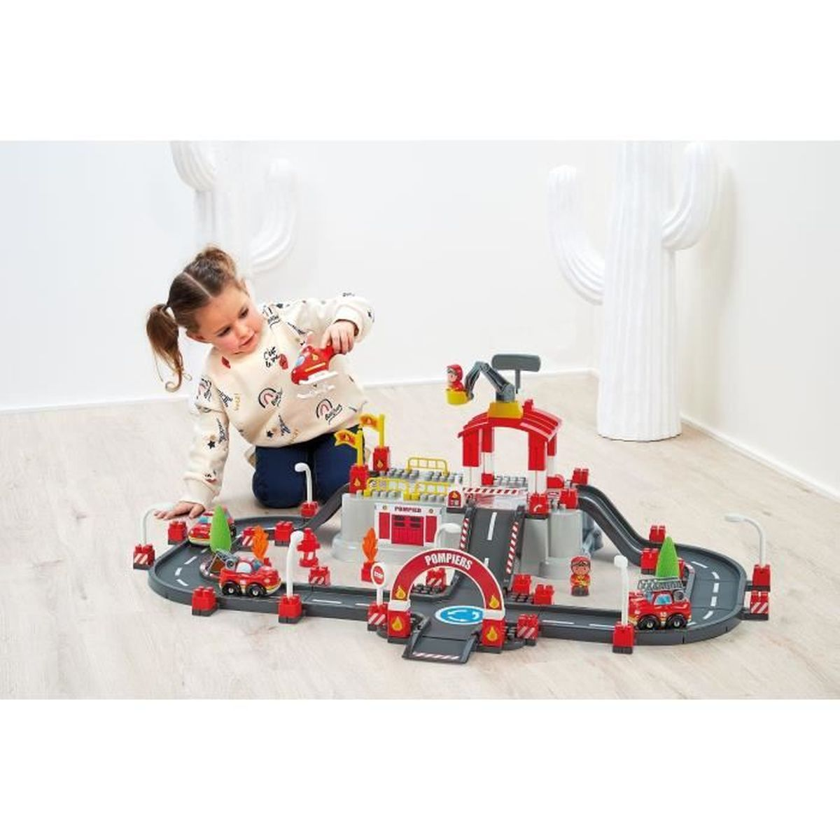 Ein kleines Mädchen spielt mit einem Spielzeug-Feuerwehrhaus und Autos.