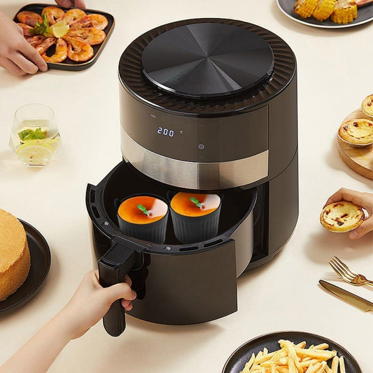 Eine schwarze Heißluftfritteuse mit zwei Tassen cremiger Nachspeise, umgeben von Lebensmitteln.