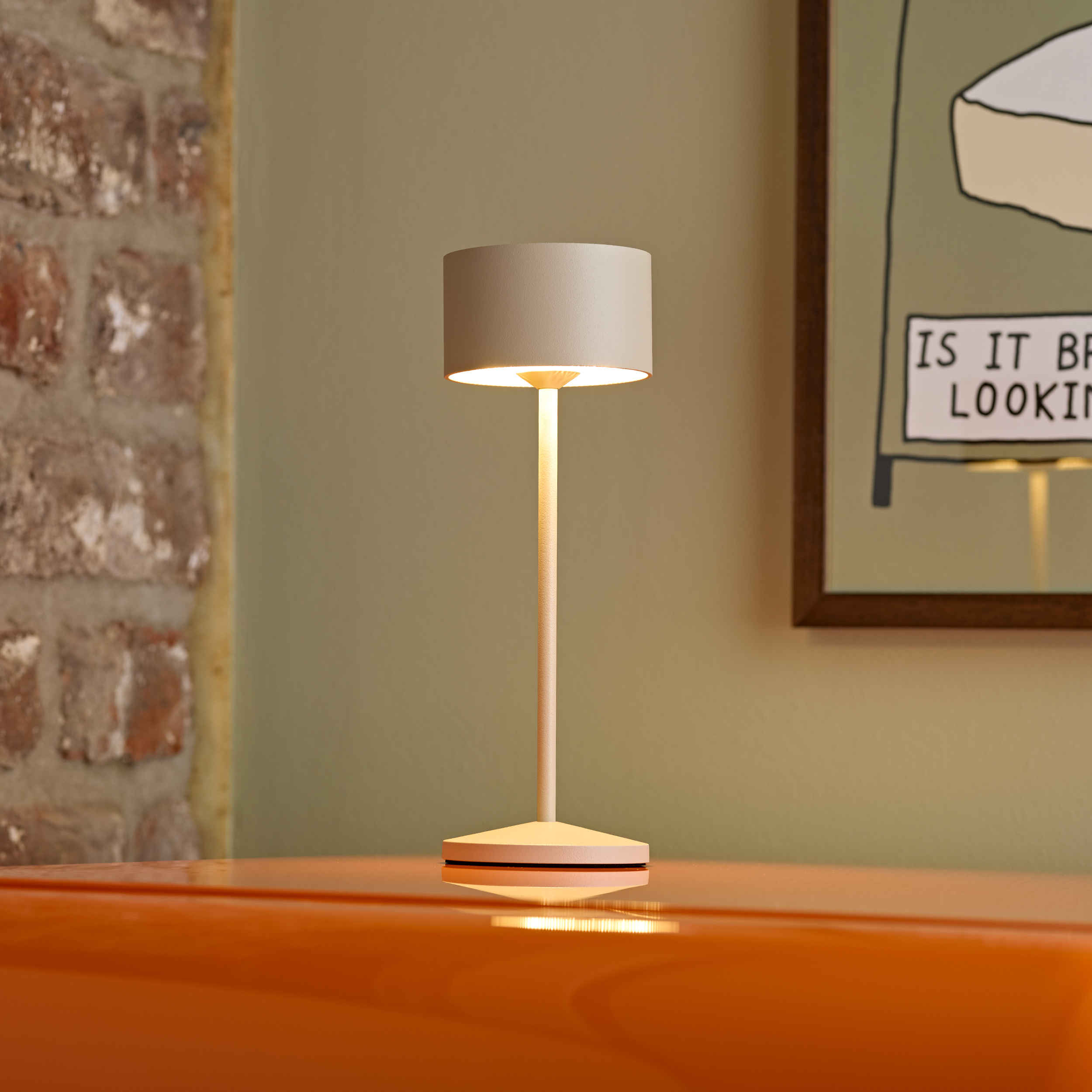 Eine schlichte, cremefarbene Tischlampe steht auf einer glänzenden orangefarbenen Oberfläche.