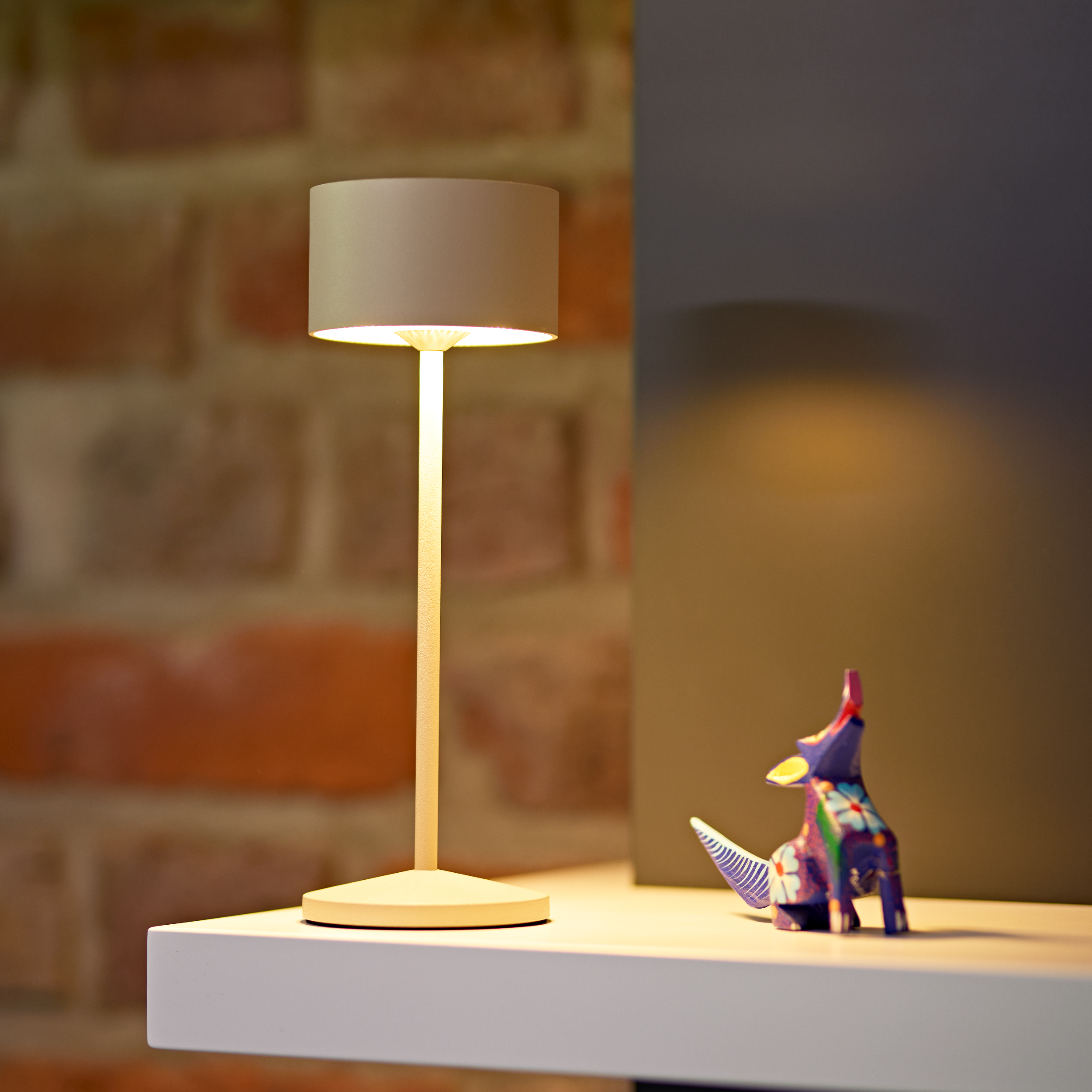 Eine beige Lampe und eine bunte Tierfigur auf einem Regal.
