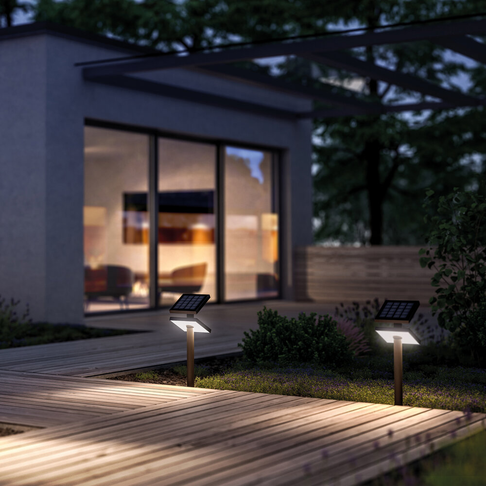 Zwei Solarleuchten beleuchten einen Holzweg vor einem modernen Haus im Abendlicht.
