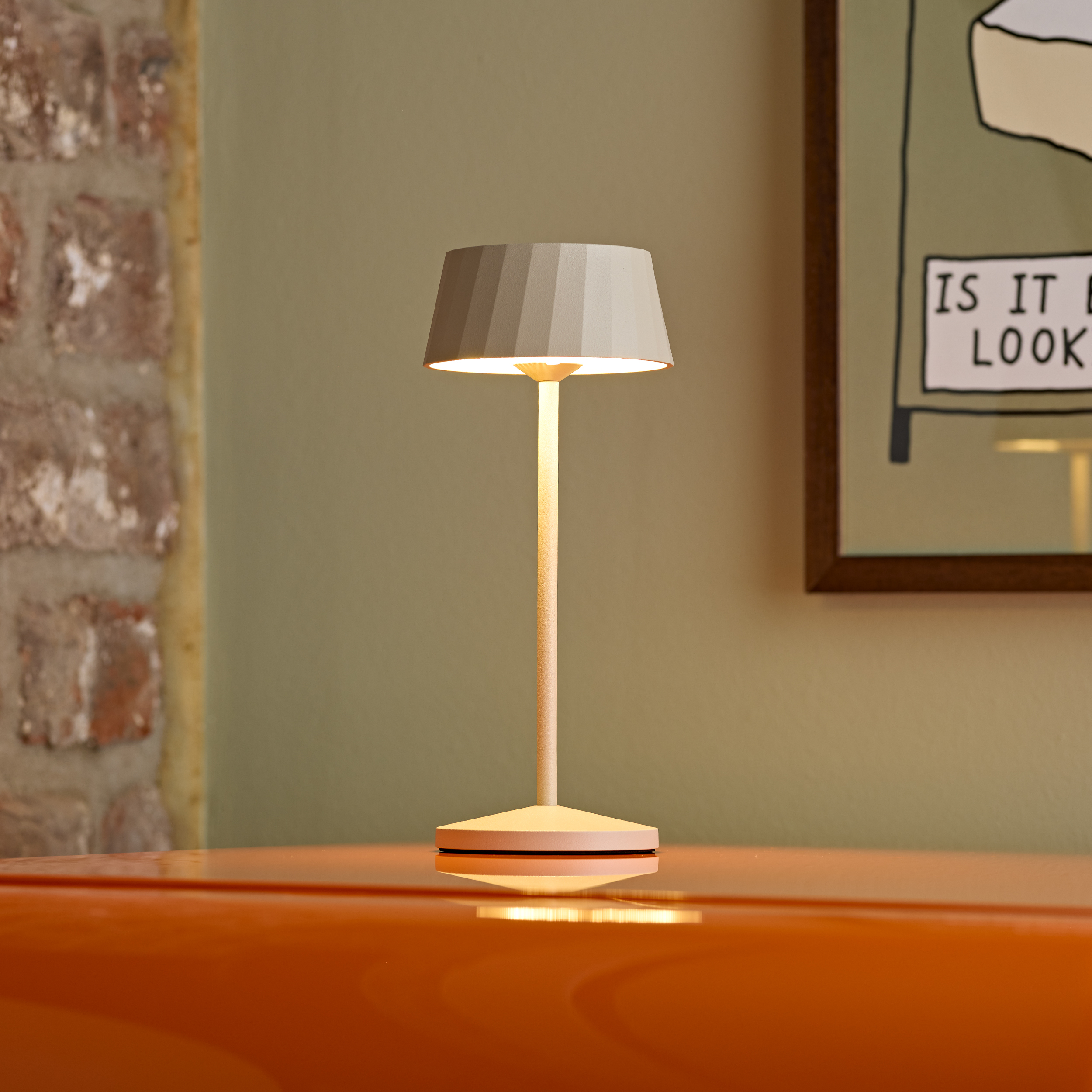 Eine moderne Lampe steht auf einem orangefarbenen Tisch. Backsteinwand im Hintergrund.