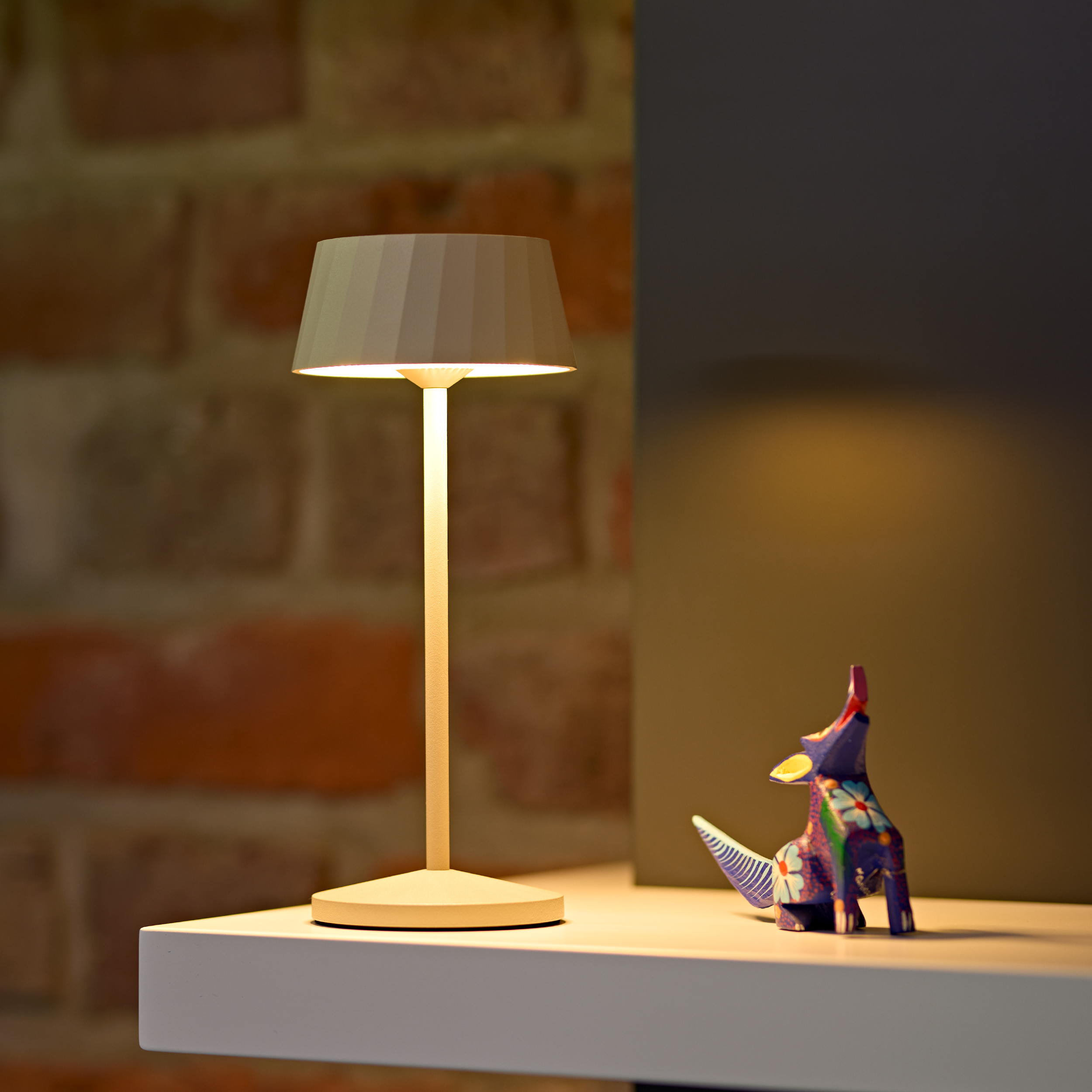 Eine Lampe und eine bunte Tierfigur auf einem Regal vor einer Ziegelwand.