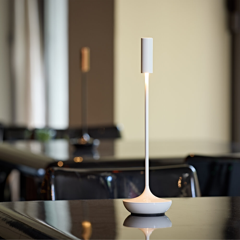 Eine weiße Lampe auf einem Tisch mit einem verschwommenen Hintergrund von Stühlen.