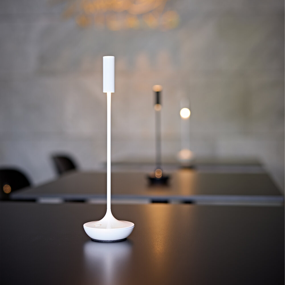 Eine weiße Schreibtischlampe steht auf einem schwarzen Tisch, drei weitere Lampen im Hintergrund.