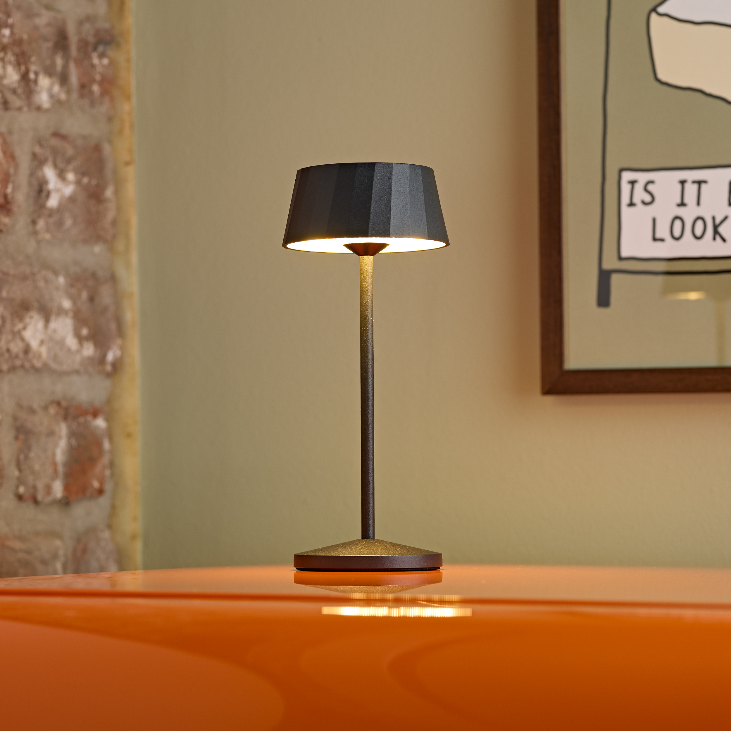 Eine schwarze Lampe auf einem orangefarbenen Tisch vor einer Ziegelwand.