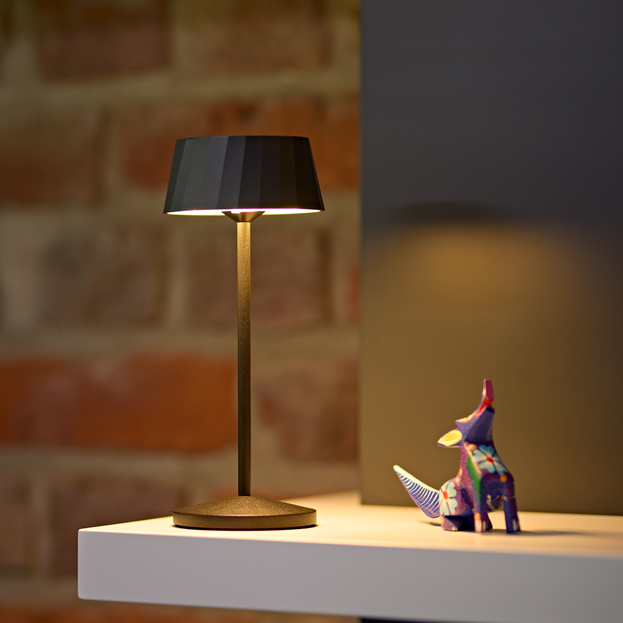 Eine schwarze Lampe auf einem Regal neben einer bunten Tierfigur.