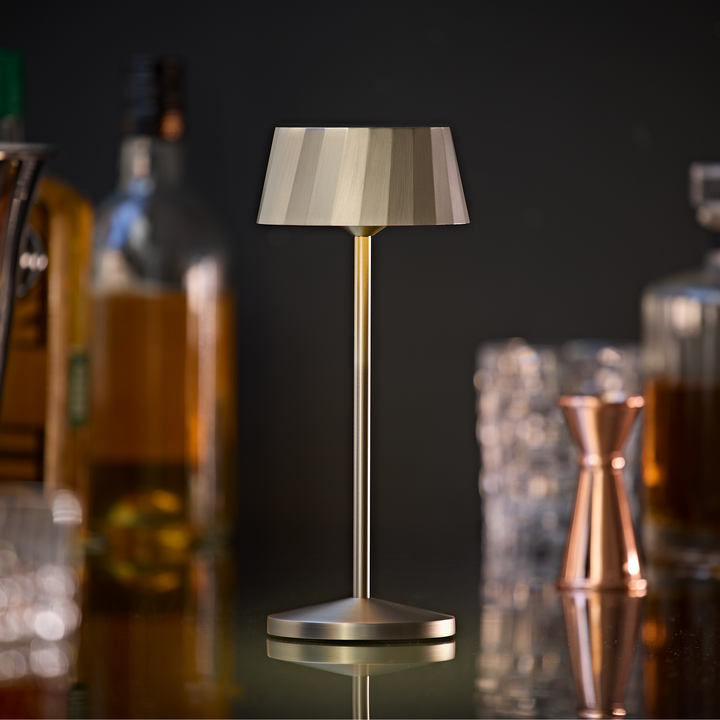 Eine Tischlampe mit gestreiftem Schirm steht auf einem Tisch mit Flaschen im Hintergrund.