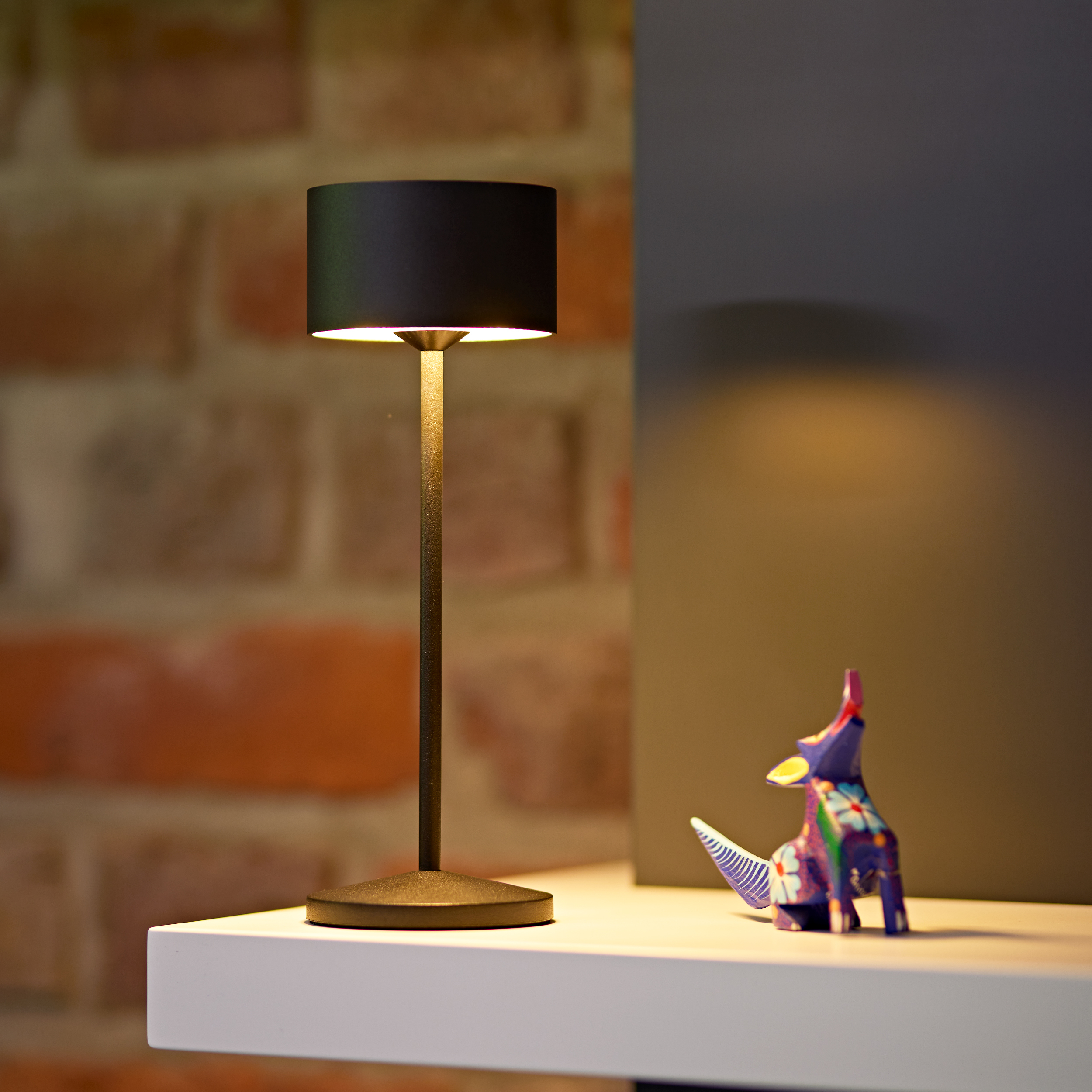 Eine schwarze Lampe und eine bunte Tierfigur stehen auf einem Regal.