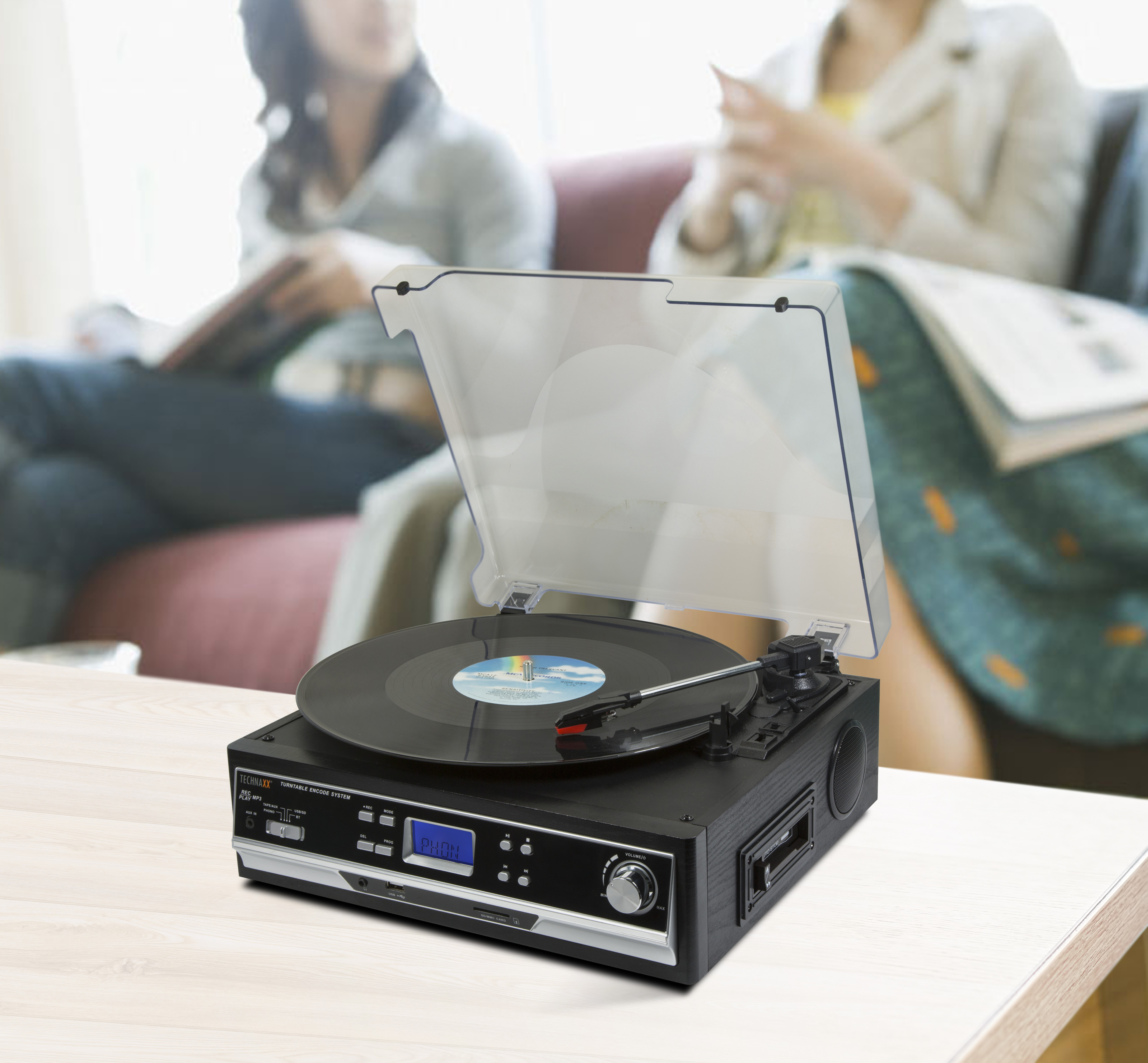 Tocadiscos negro con disco de vinilo, dos mujeres al fondo.