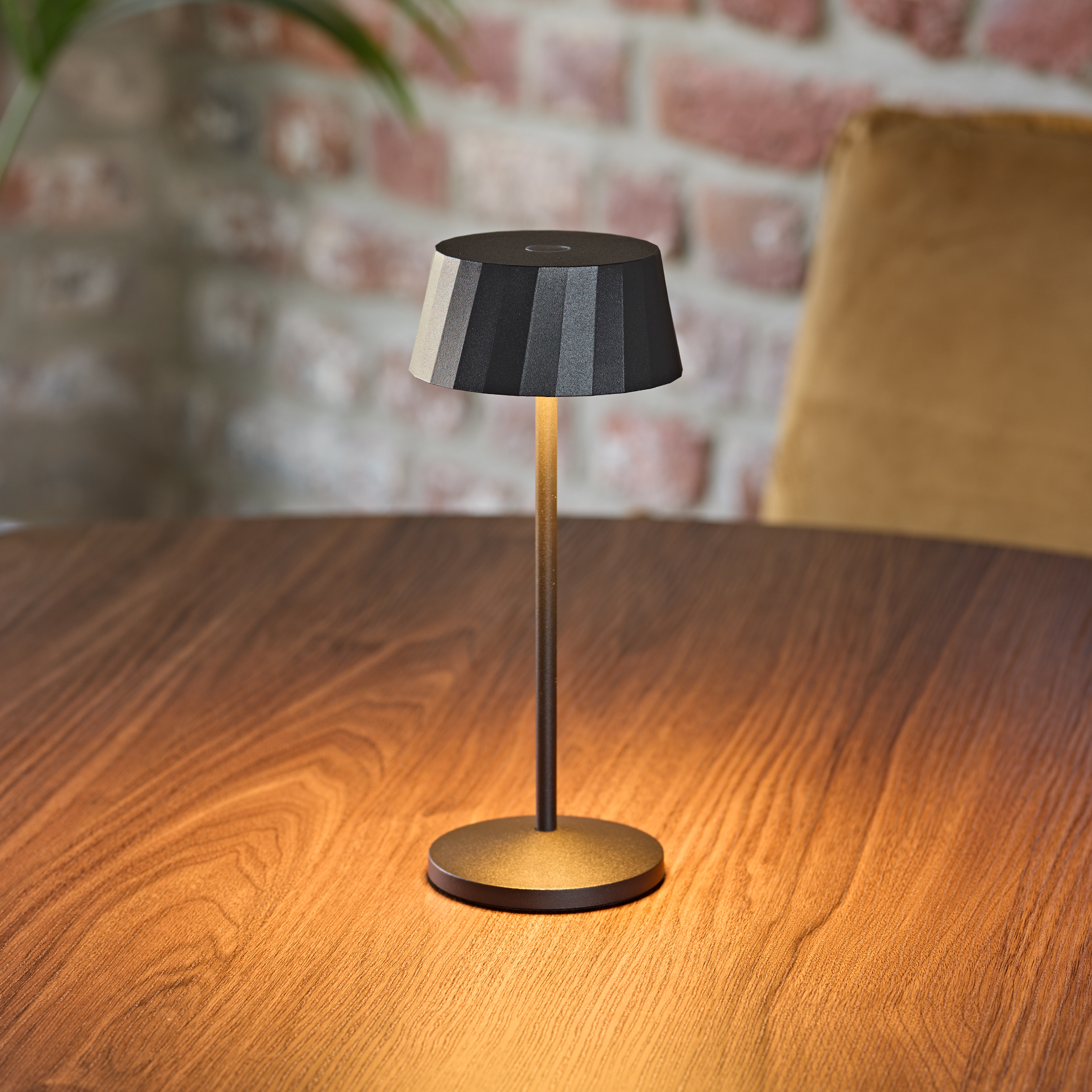 Eine schwarze Tischlampe mit geripptem Schirm steht auf einem Holztisch.
