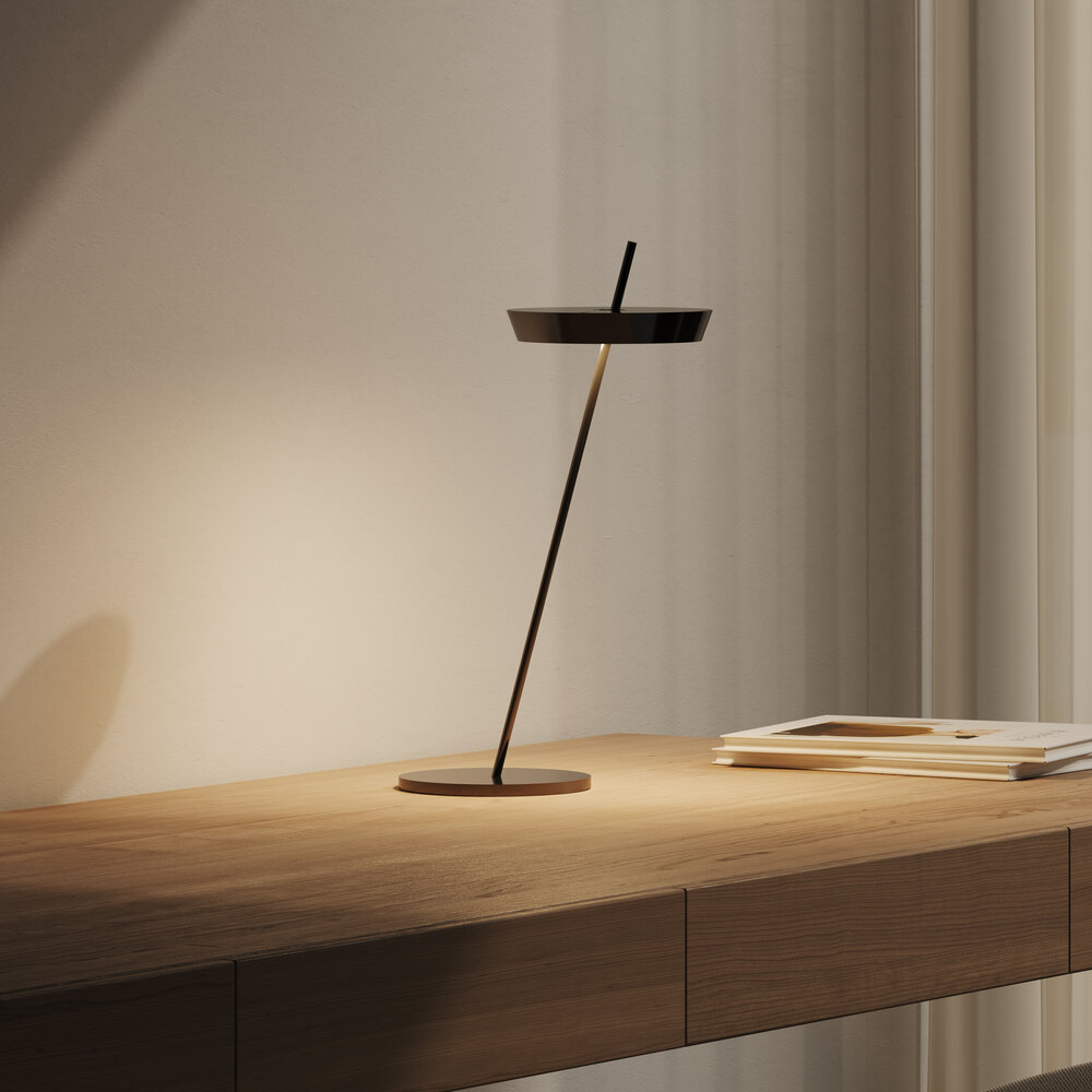 Eine dunkle Schreibtischlampe mit schmalem Ständer steht auf einem Holztisch.