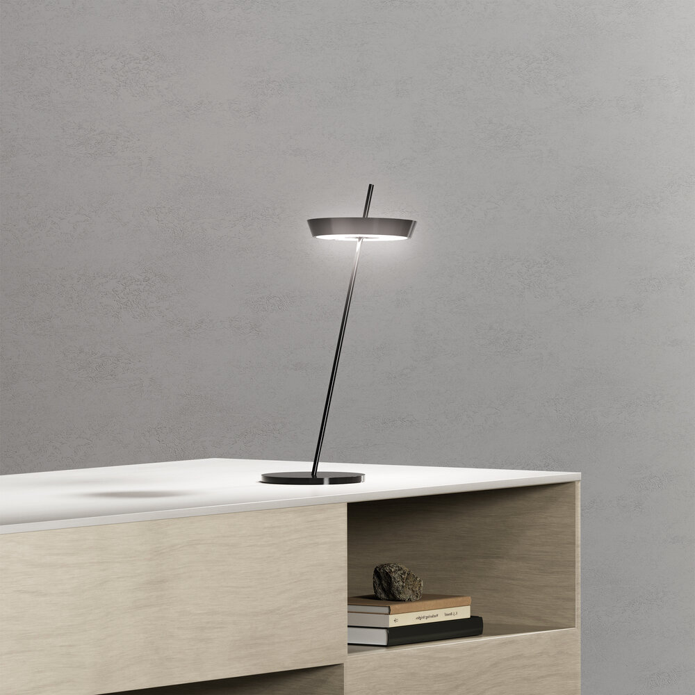 Eine moderne Tischlampe mit schlankem Metallständer auf einem weißen Tisch.