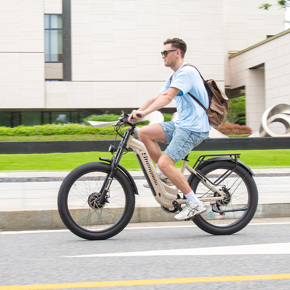 Mann fährt ein beiges E-Bike mit Rucksack auf einer Straße vor einem modernen Gebäude.