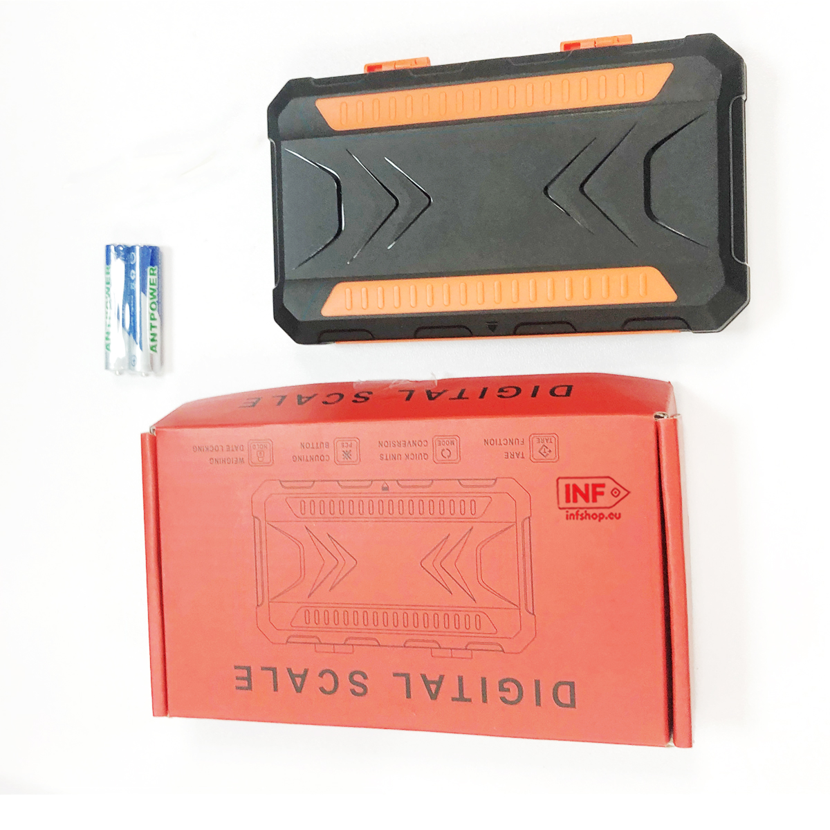 Eine Waage, zwei Batterien und eine orangefarbene Box mit Beschriftung.