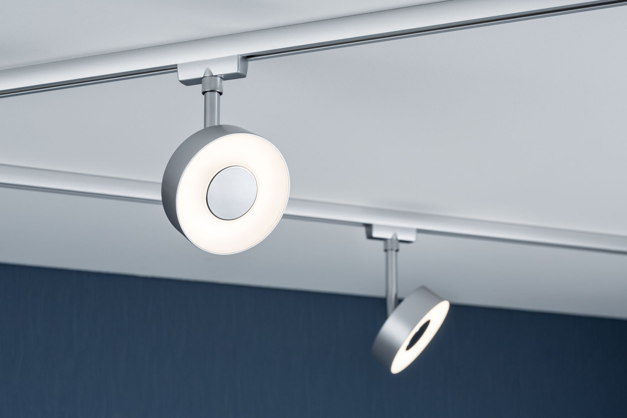 Zwei moderne silberne Deckenstrahler mit Ringen, die Licht abgeben, an einer Schiene.