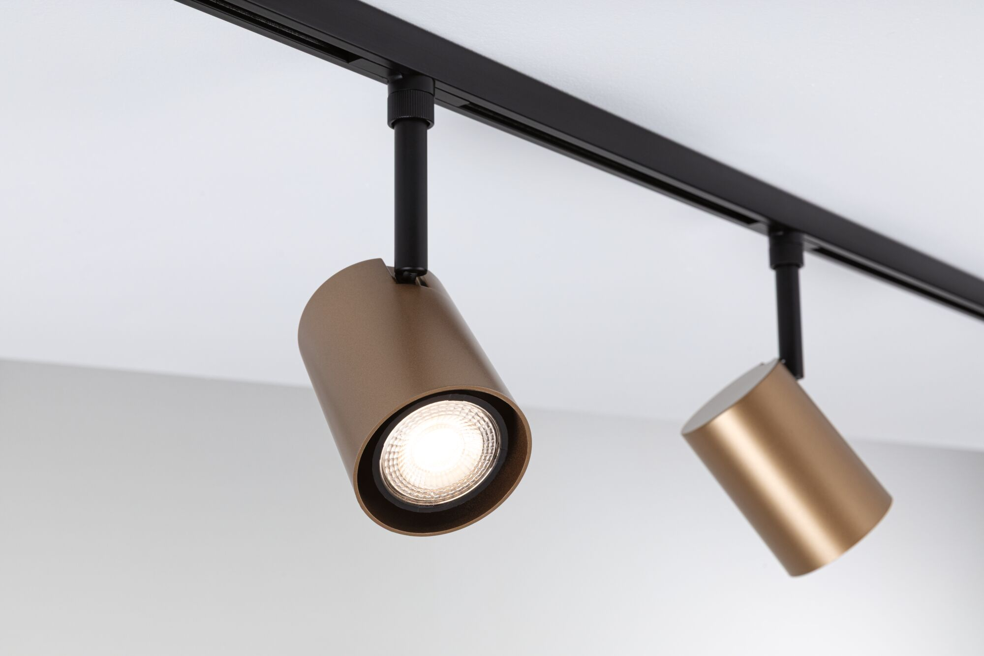Zwei bronzefarbene Zylinder-Spots an einer schwarzen Stromschiene an der Decke.