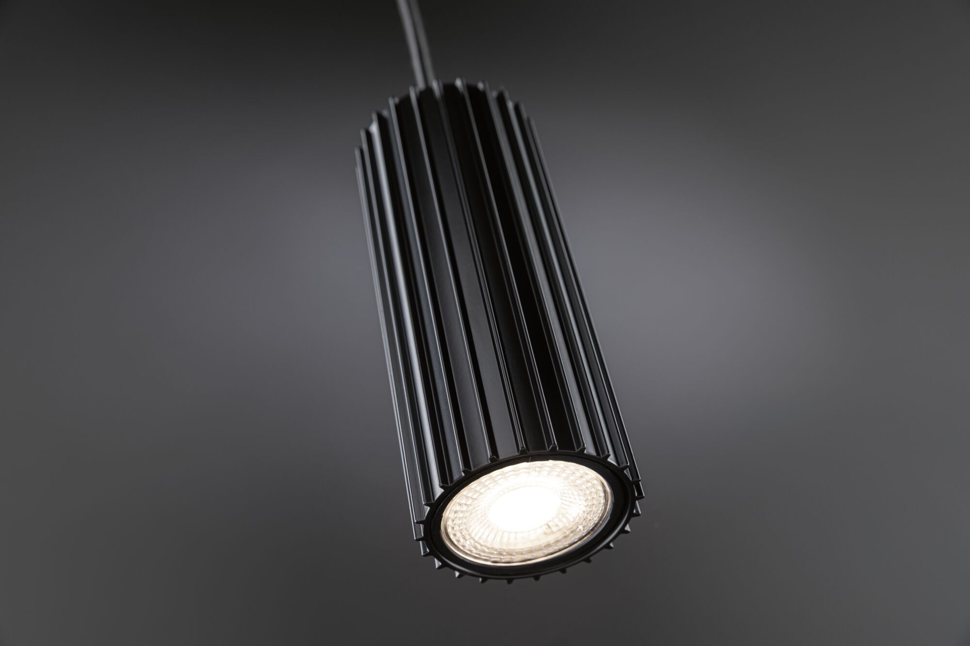 Un projecteur cylindrique noir à rainures verticales est illuminé vivement.
