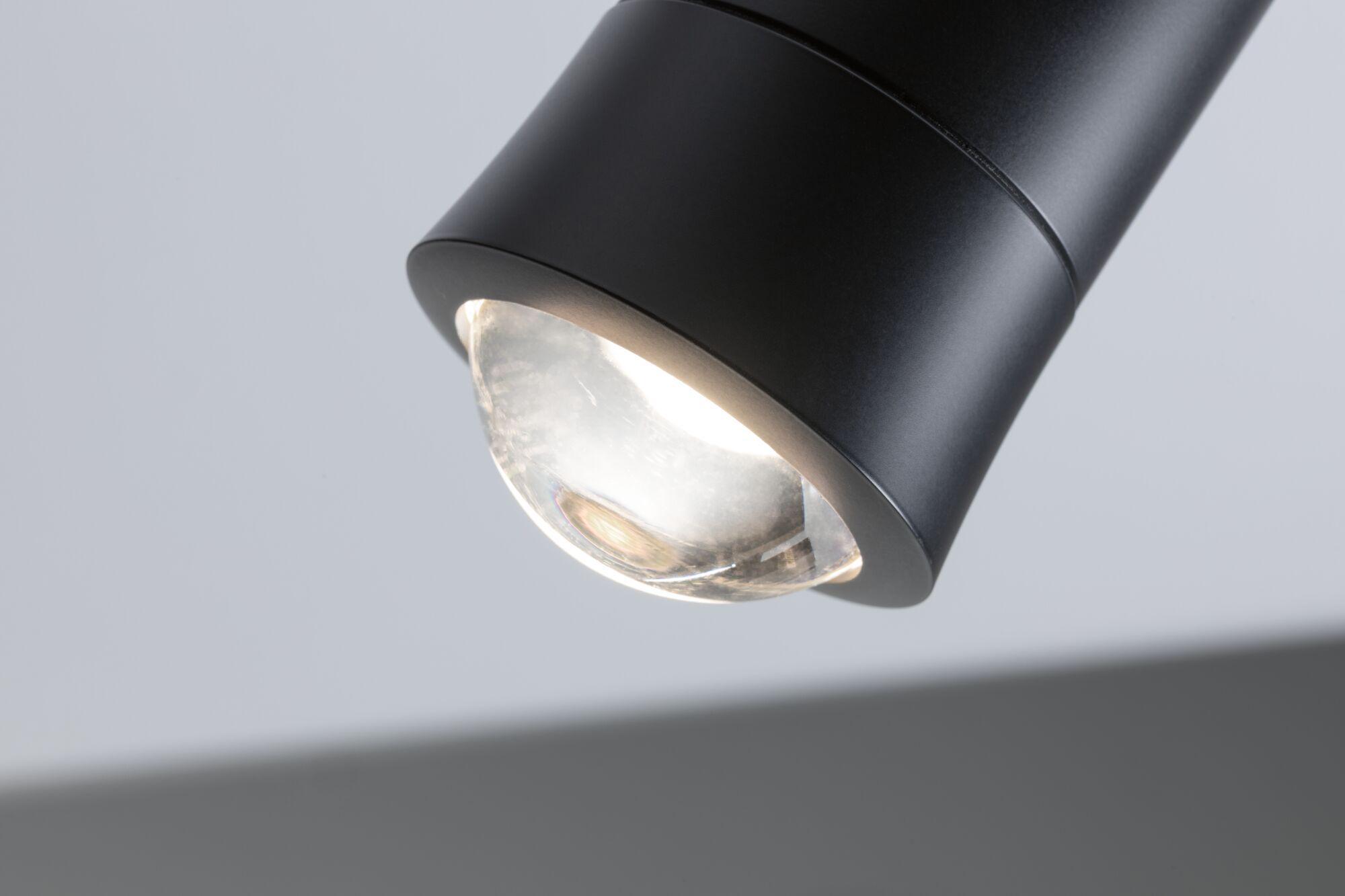 Ein schwarzer Deckenstrahler mit Glaskuppel leuchtet.
