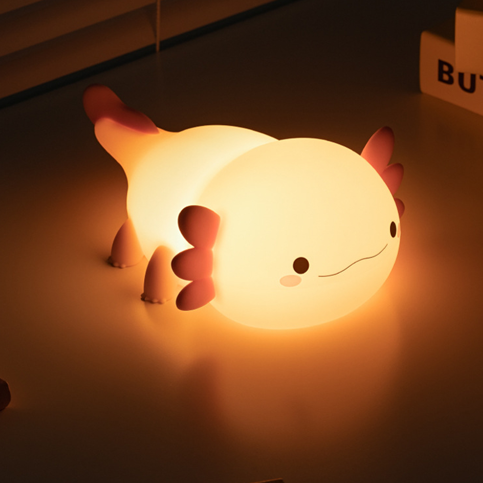 Eine leuchtende Axolotl-Lampe mit niedlichem Gesicht liegt auf einer dunklen Oberfläche.