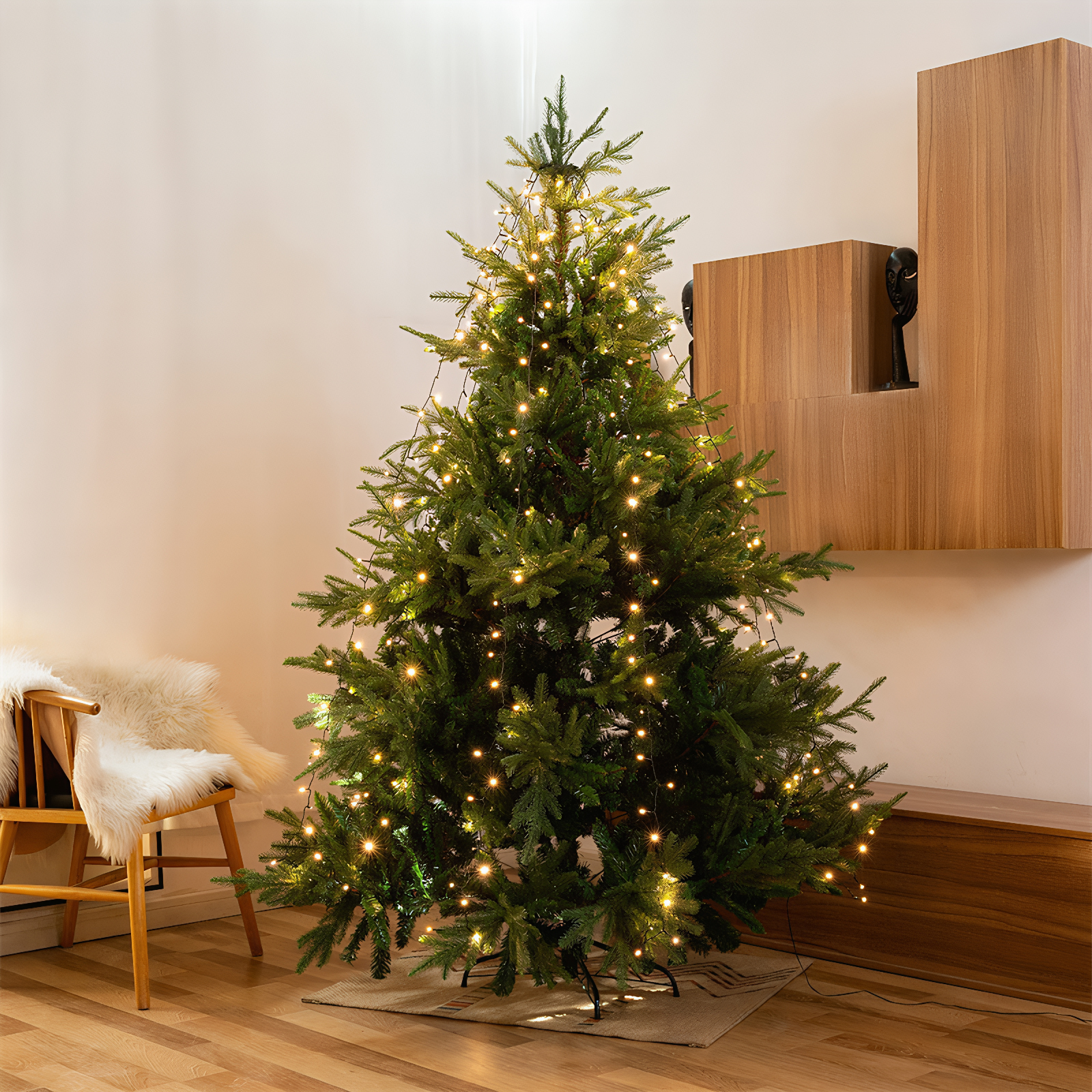 Ein grüner Weihnachtsbaum mit warmweißen Lichtern steht in einem Raum mit Holzmöbeln.