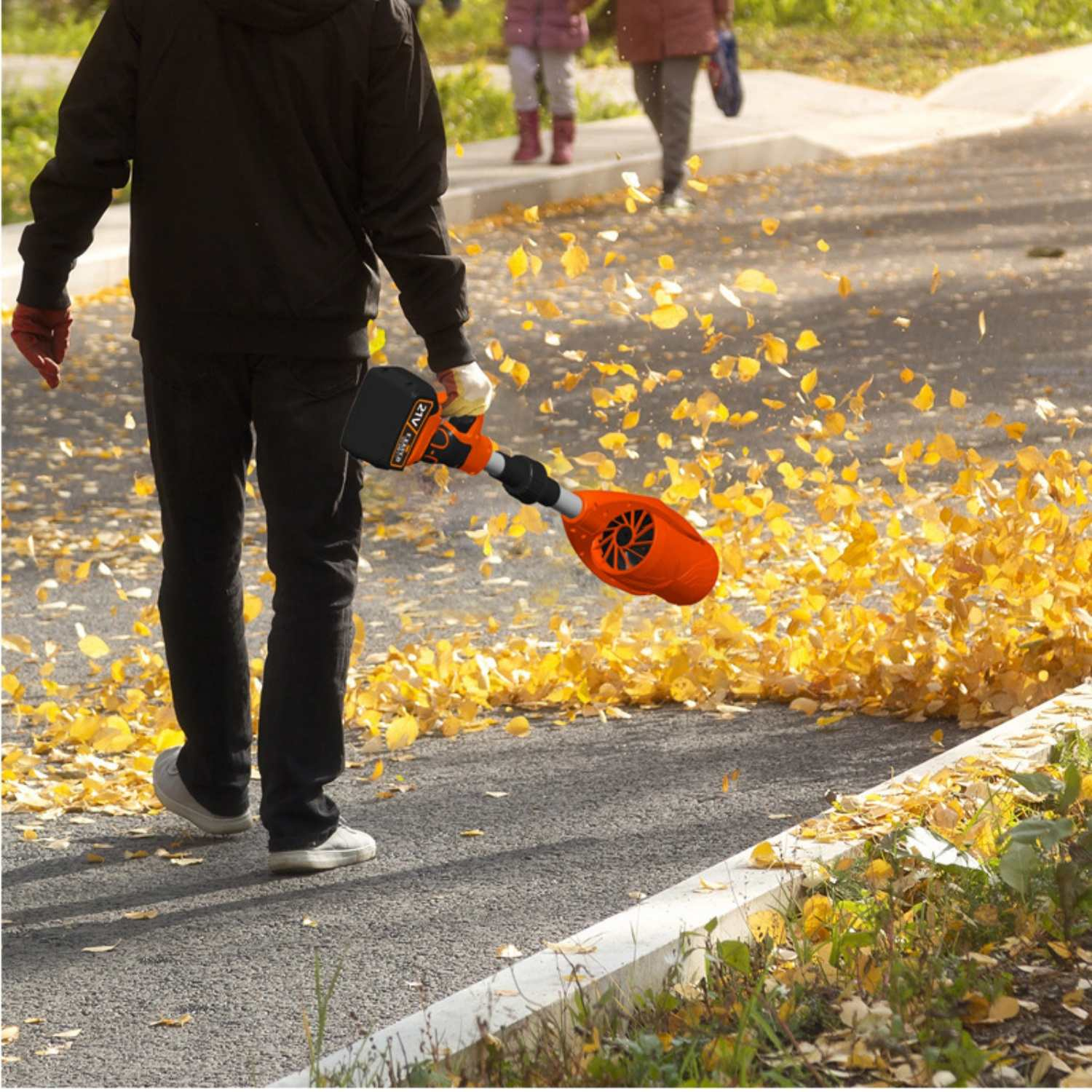 Mann fegt Herbstlaub mit einem Laubbläser, der Gelb und Orange ist.