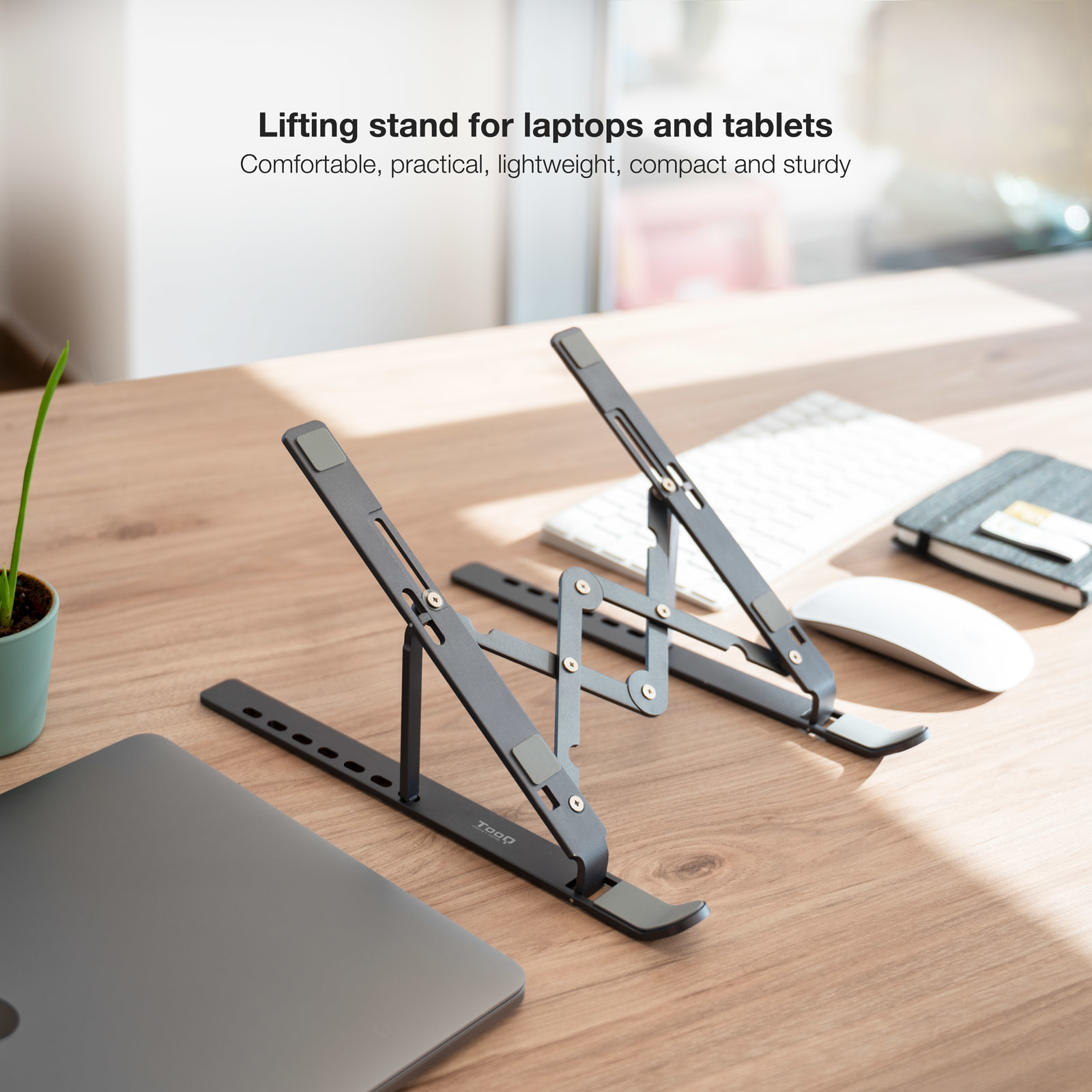 Grauer Laptopständer auf einem Holztisch mit Tastatur und Maus.