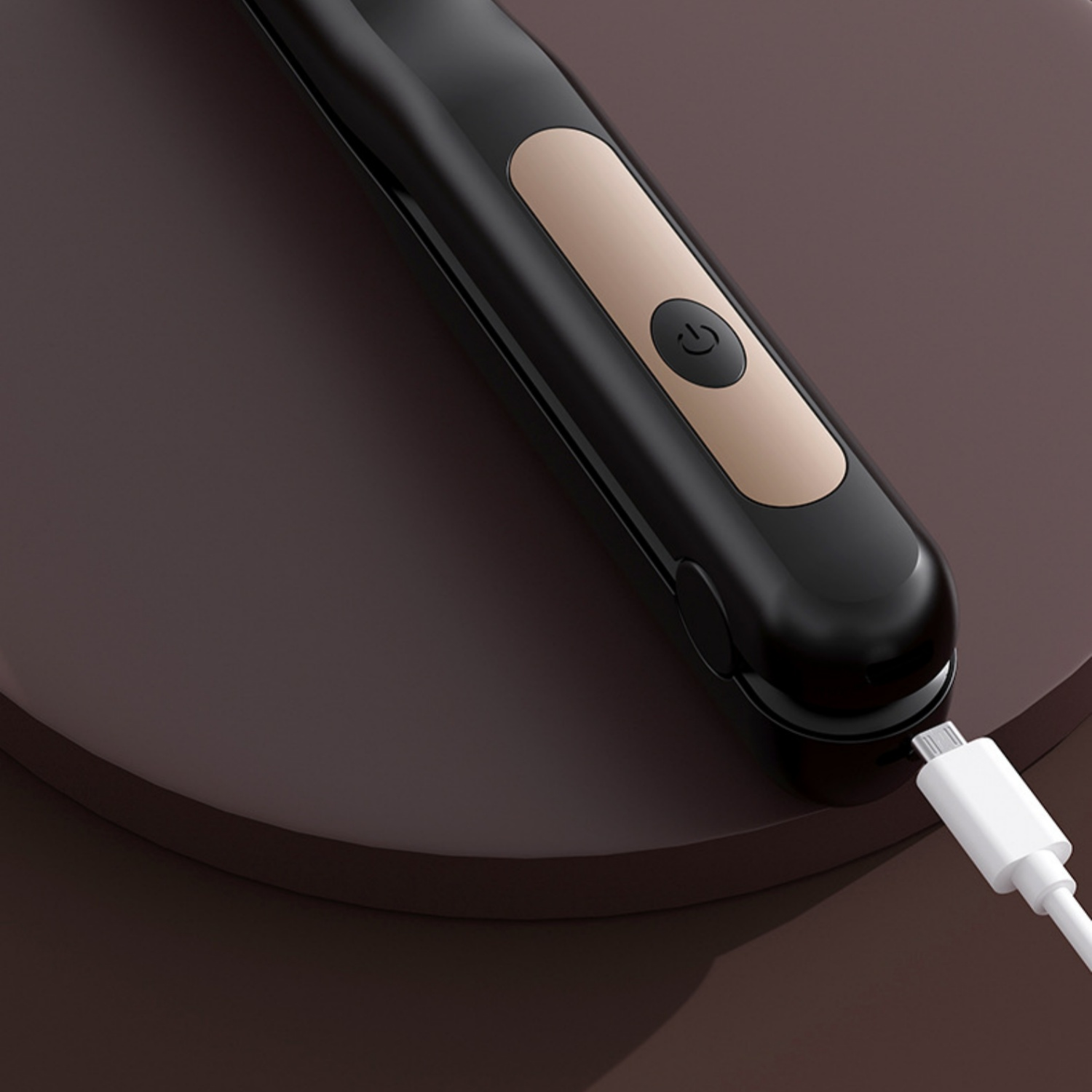 Schwarzes Gerät mit Power-Knopf lädt über USB-Kabel auf einem braunen Podest.
