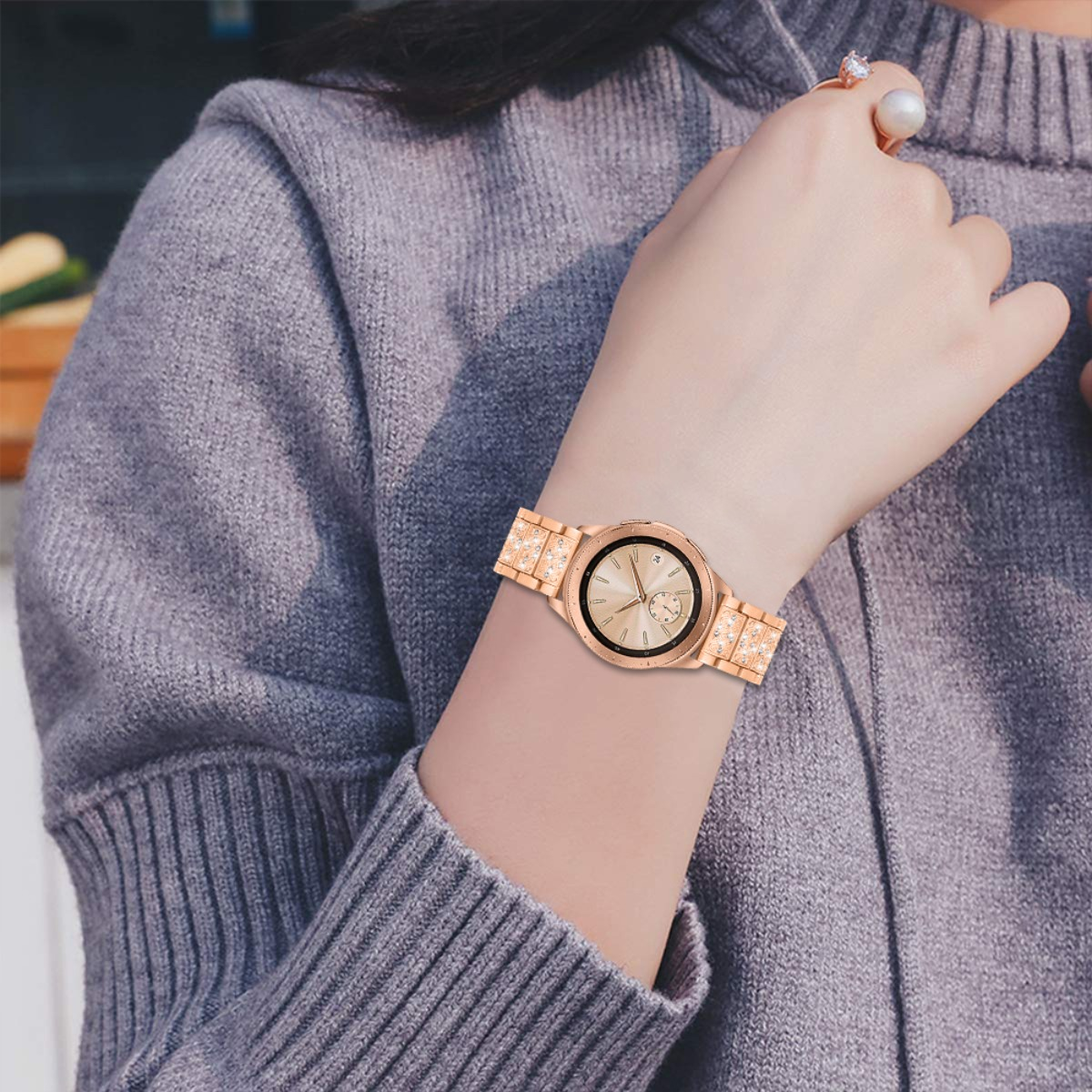 Una donna indossa uno smartwatch oro rosa con cinturino scintillante e maglione grigio.