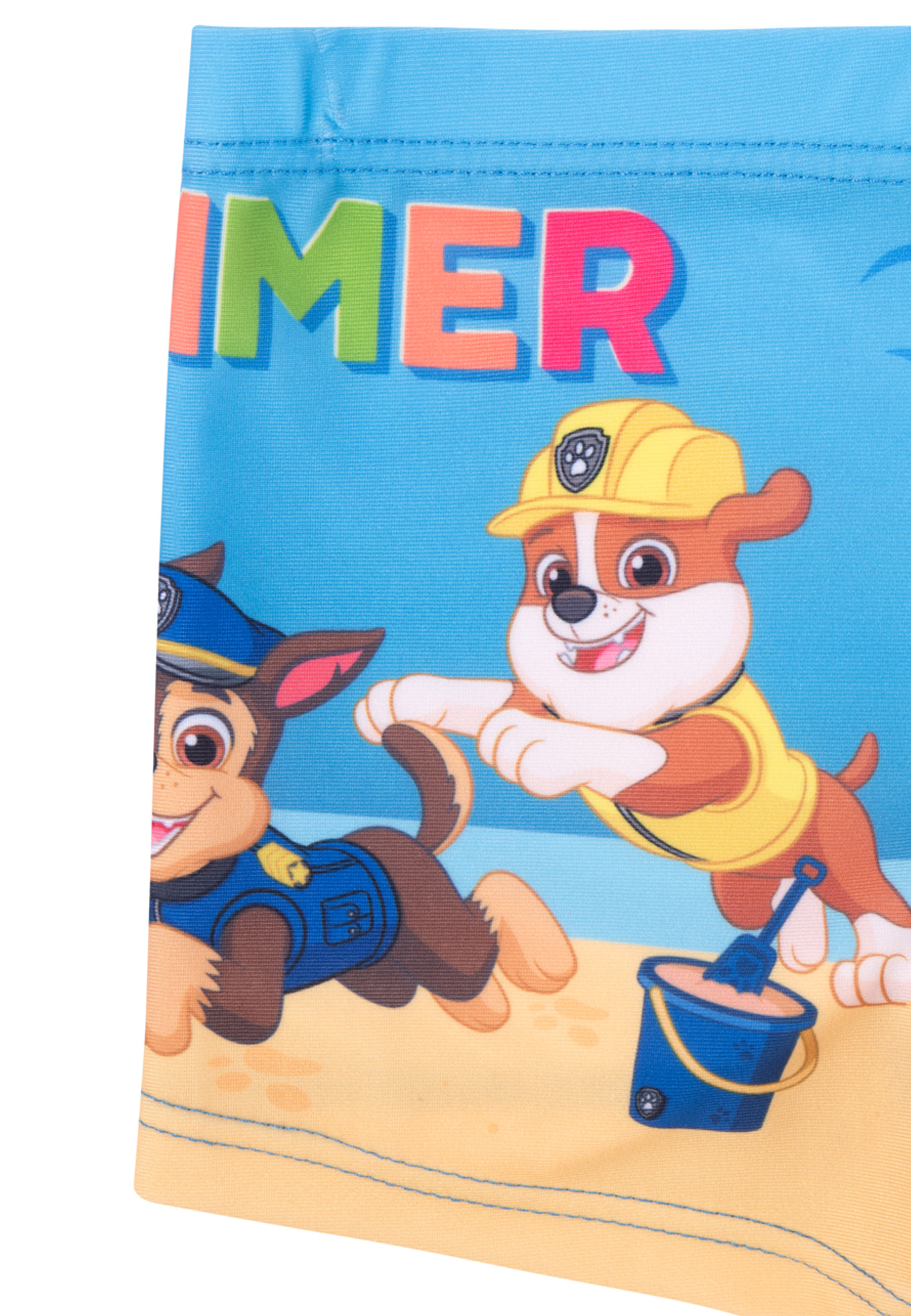 Zwei Paw Patrol Hunde, Chase und Rubble, spielen am Strand mit einem blauen Eimer und einer Schaufel.