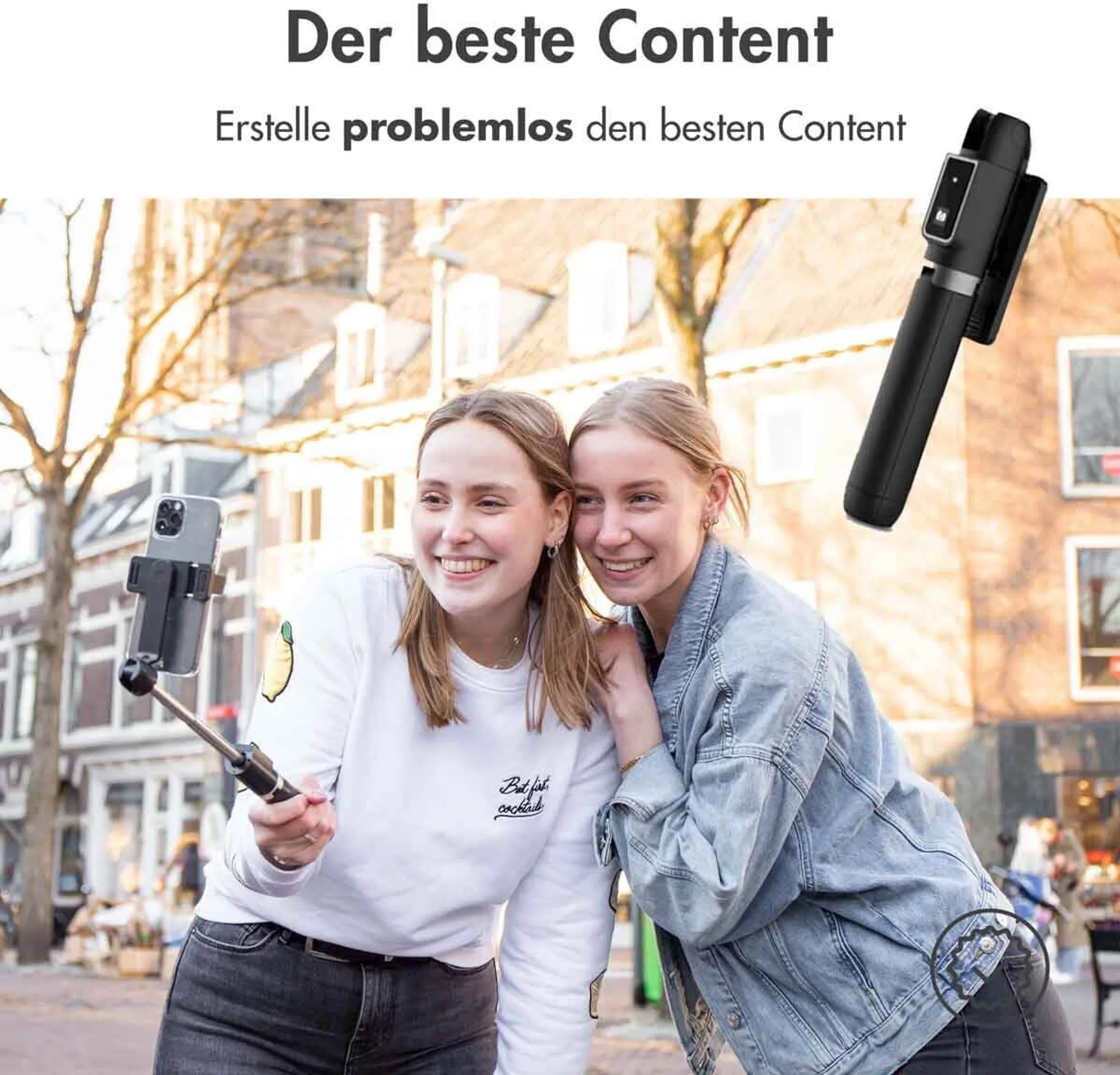 Zwei junge Frauen machen ein Selfie mit einem Selfie-Stick in einer belebten Stadtstraße.
