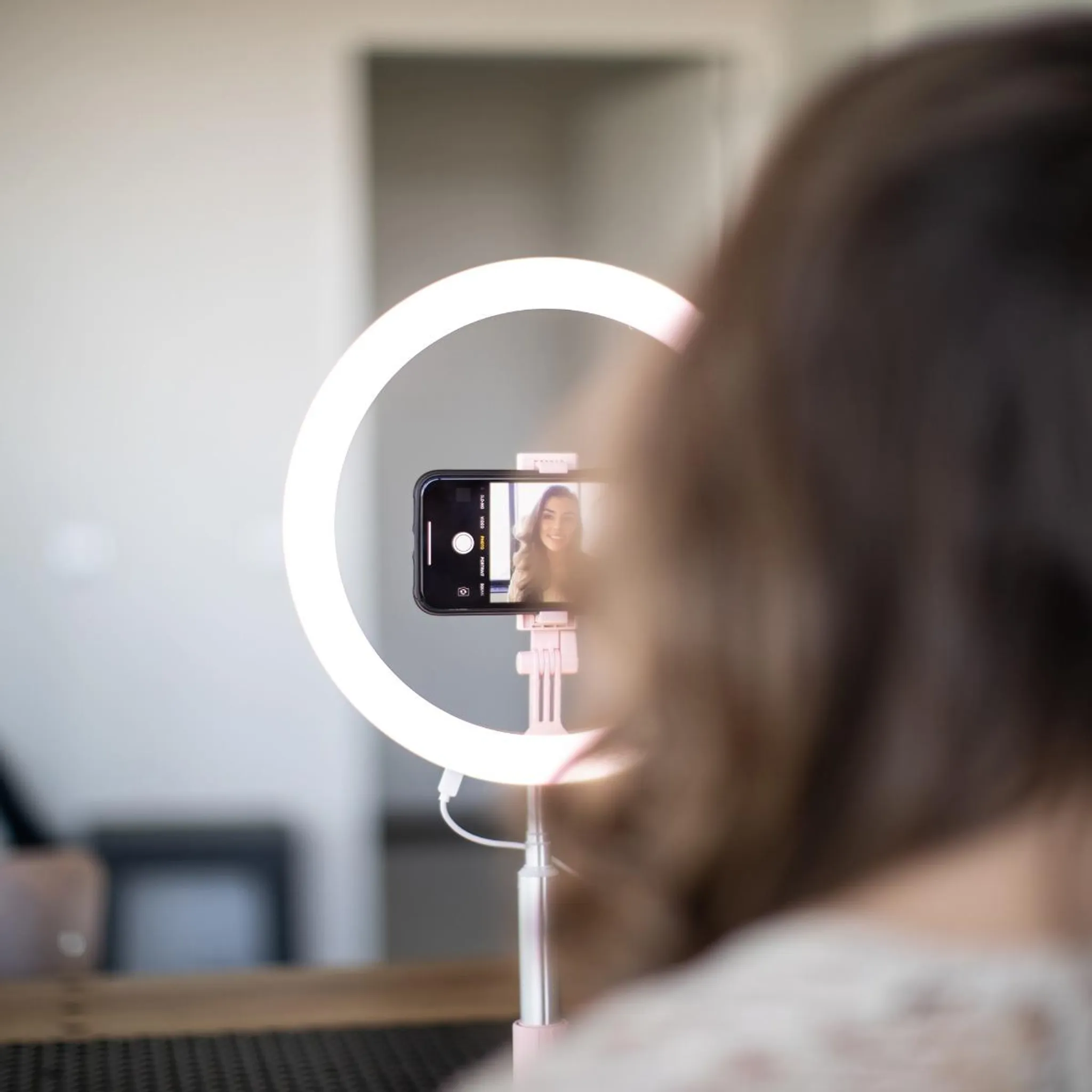 Eine Frau macht ein Selfie mit einem Ringlicht und einem Smartphone.