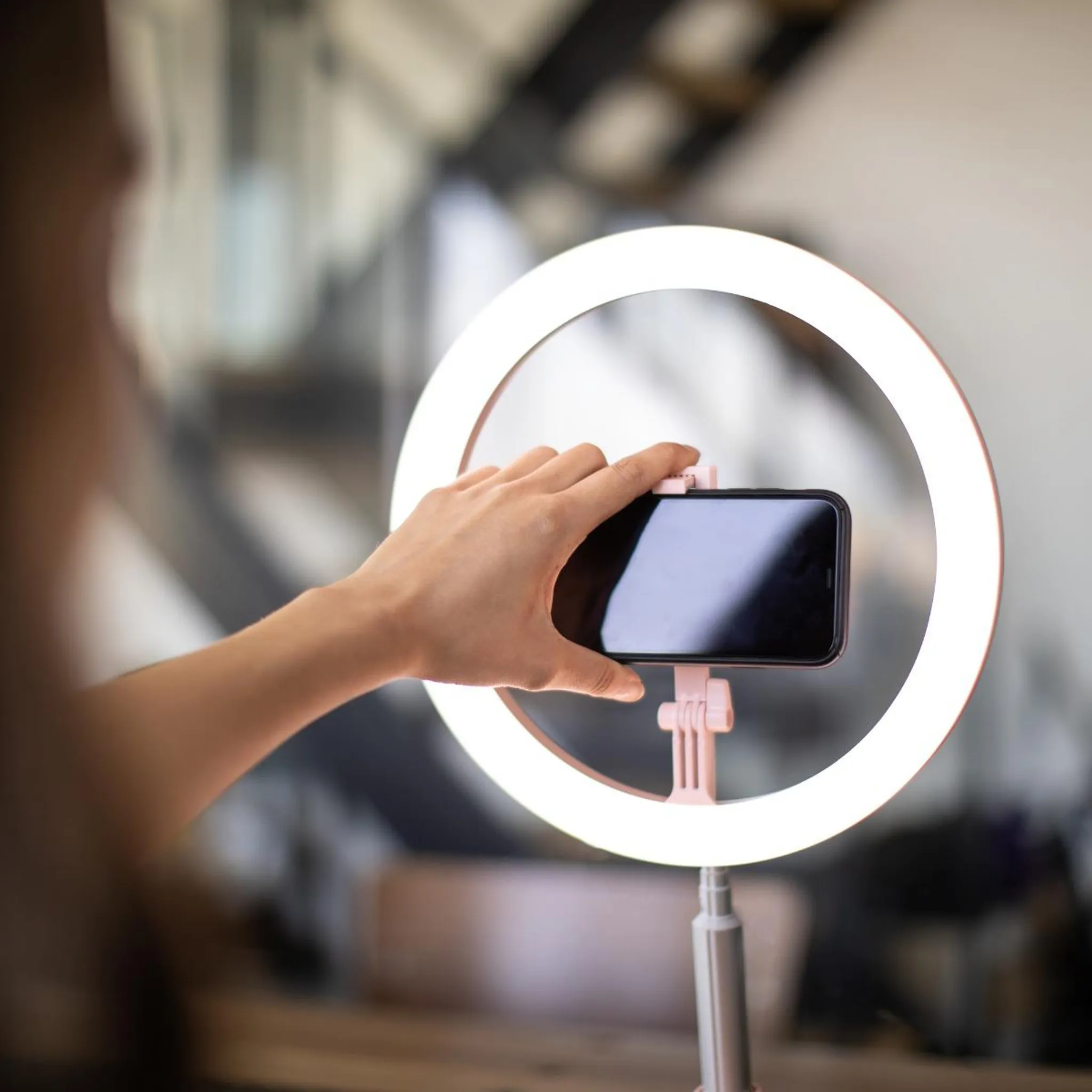 Eine Hand hält ein Smartphone vor einem leuchtenden Ringlicht. Hintergrund unscharf.