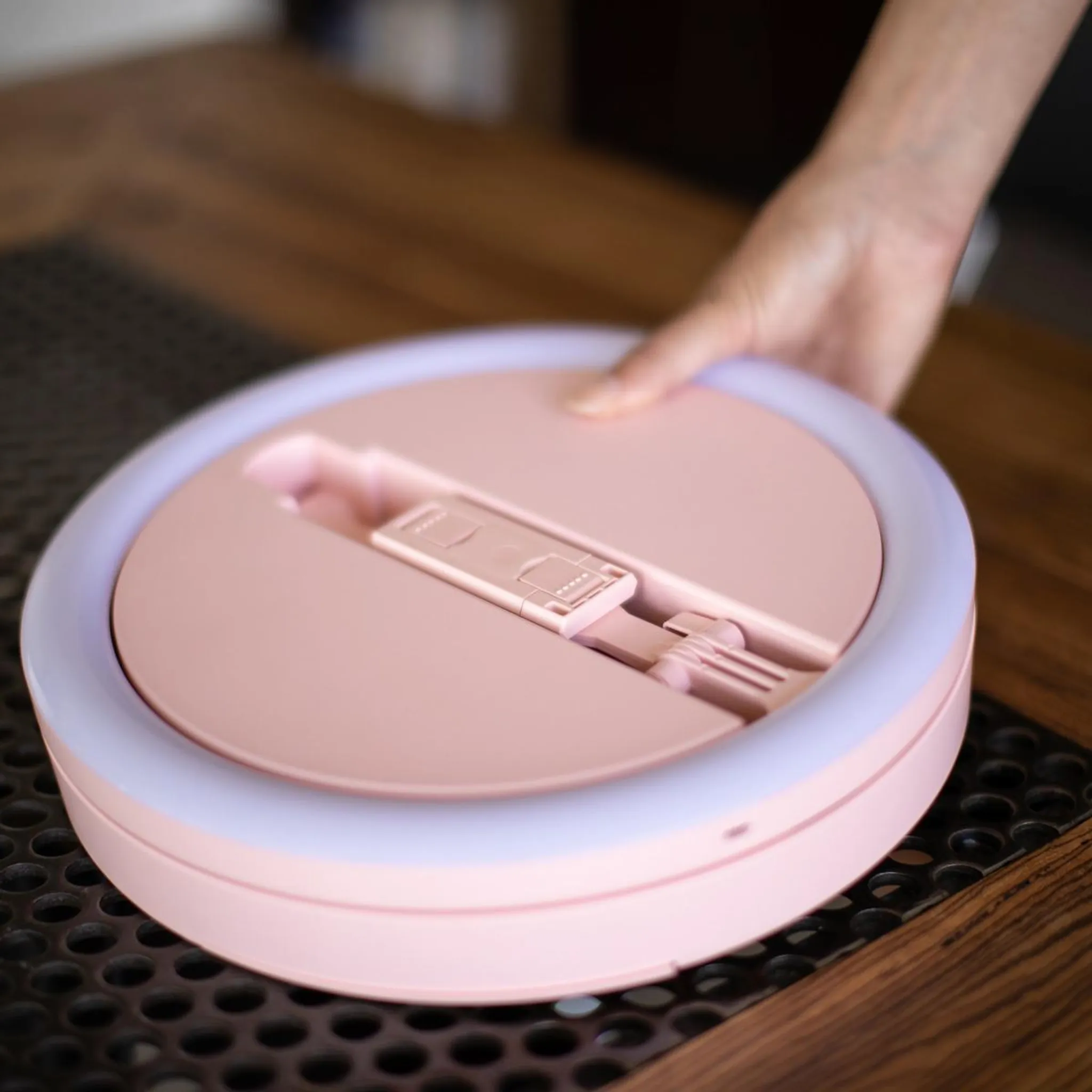 Eine Person hält ein rundes, rosafarbenes Ringlicht mit integriertem Handyhalter.
