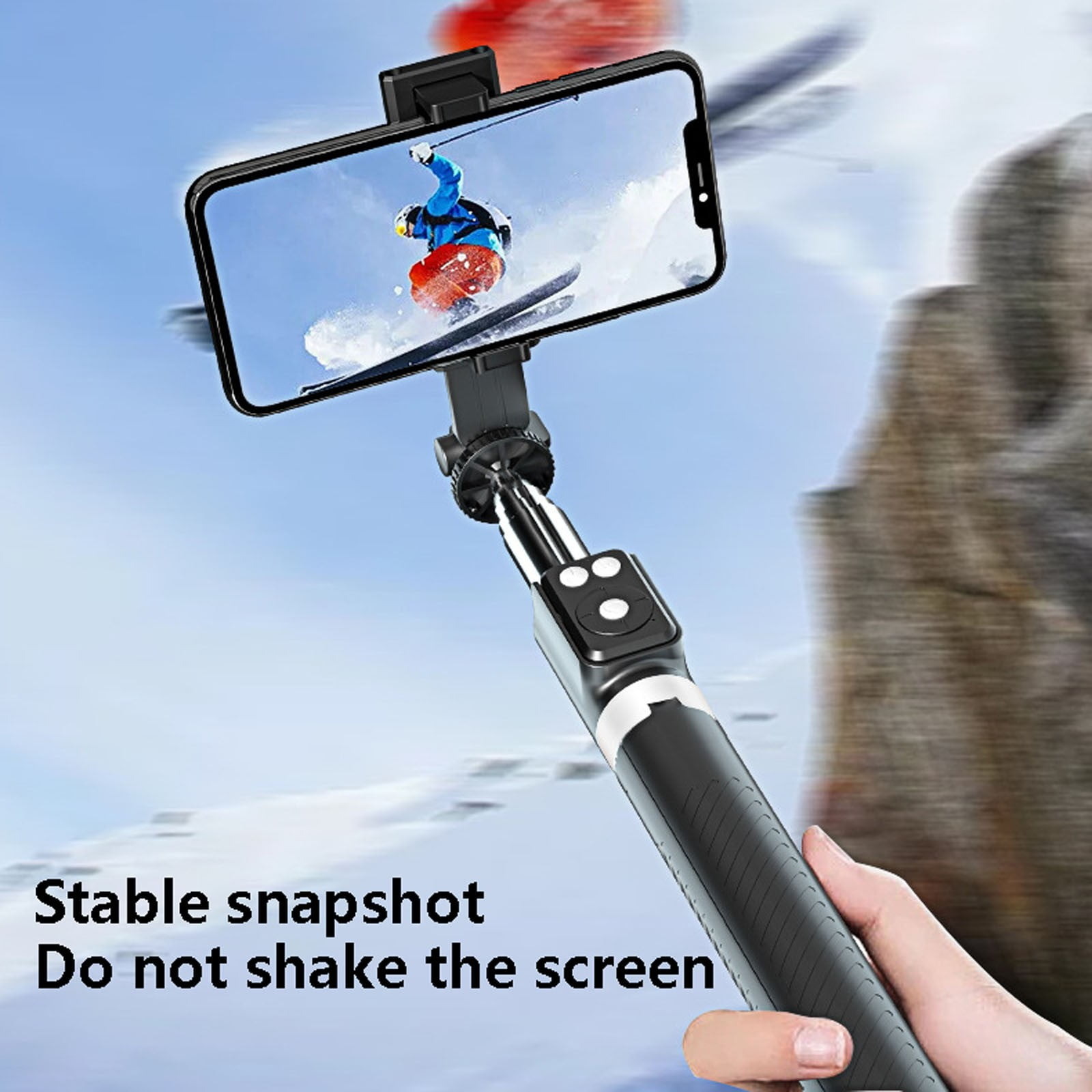 Person filmt Skifahrer mit Handy an Selfie-Stick vor verschneiter Bergkulisse.
