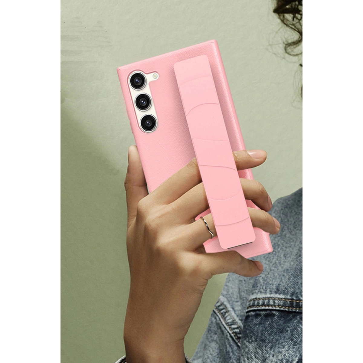 Bir el, takılı pembe tutamaçlı pembe bir akıllı telefon tutuyor.