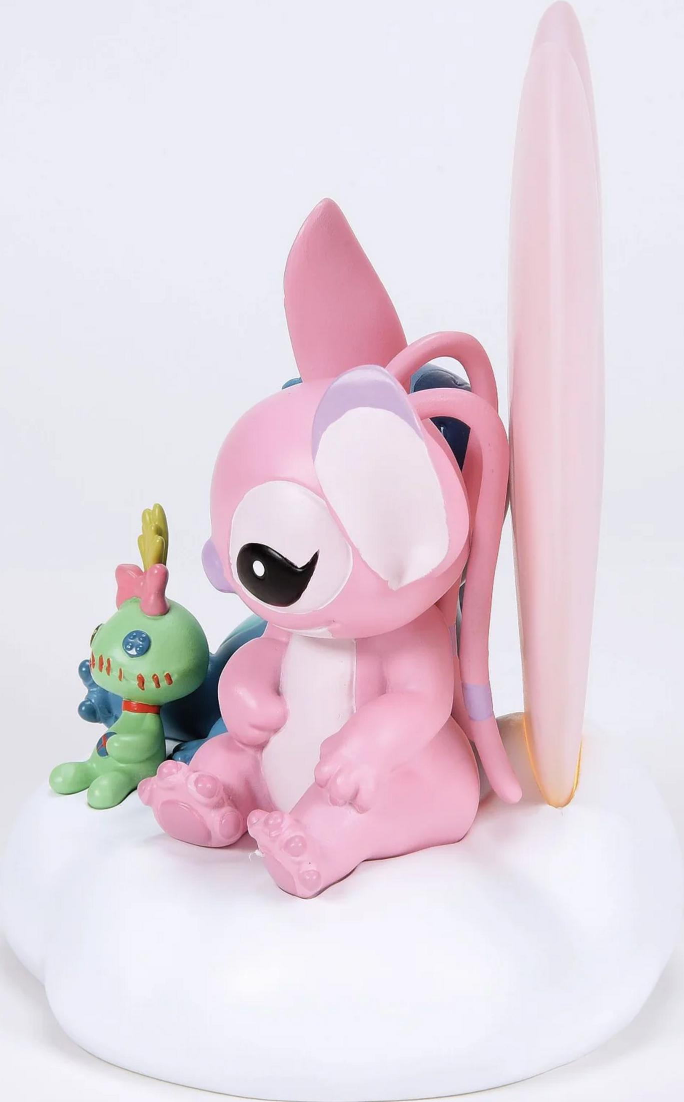 Eine rosa Figur sitzt neben einer kleinen grünen Figur und einem Surfbrett.