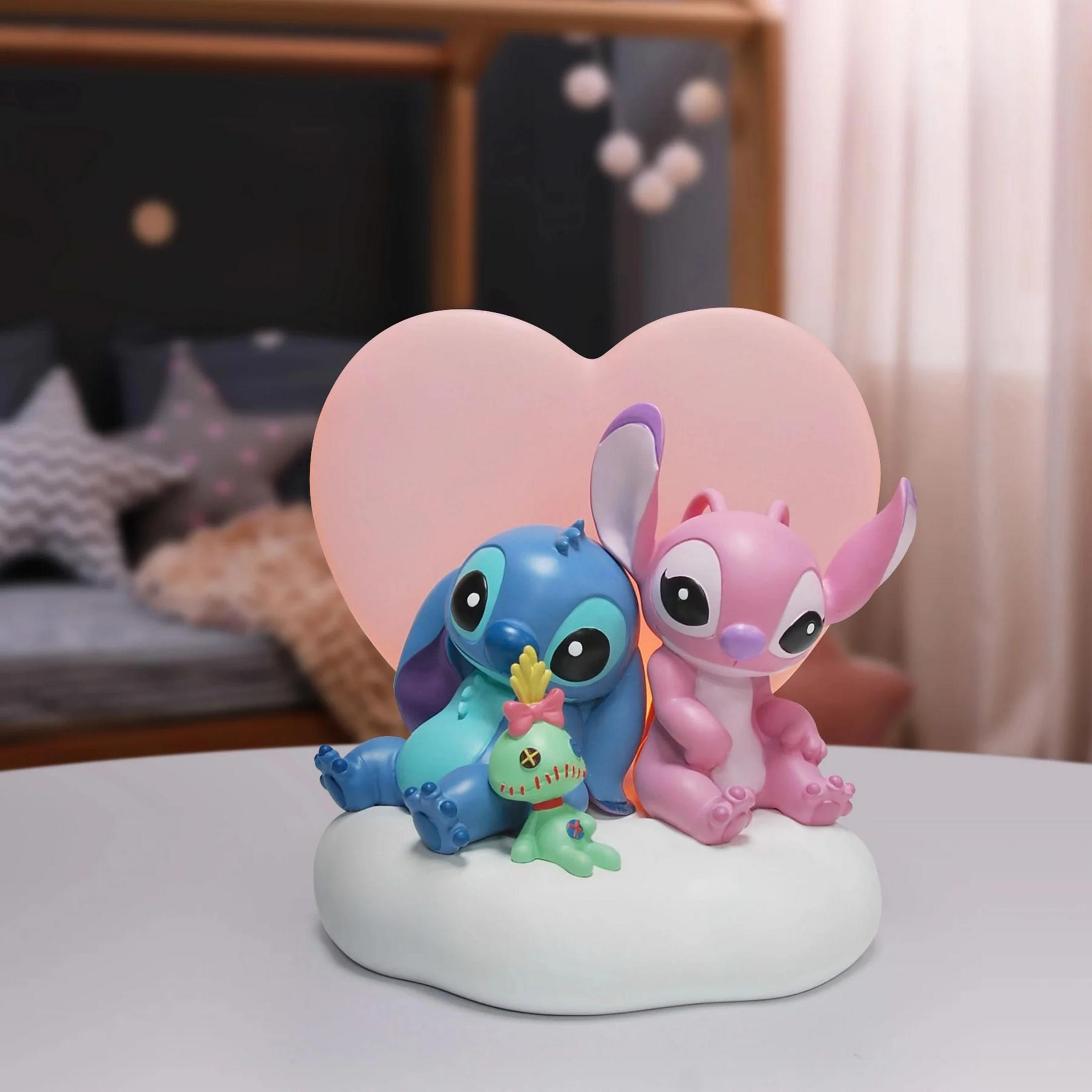 Stitch und Angel sitzen auf einer Wolke vor einem Herzlicht. Ein kleiner grüner Charakter liegt vorne.