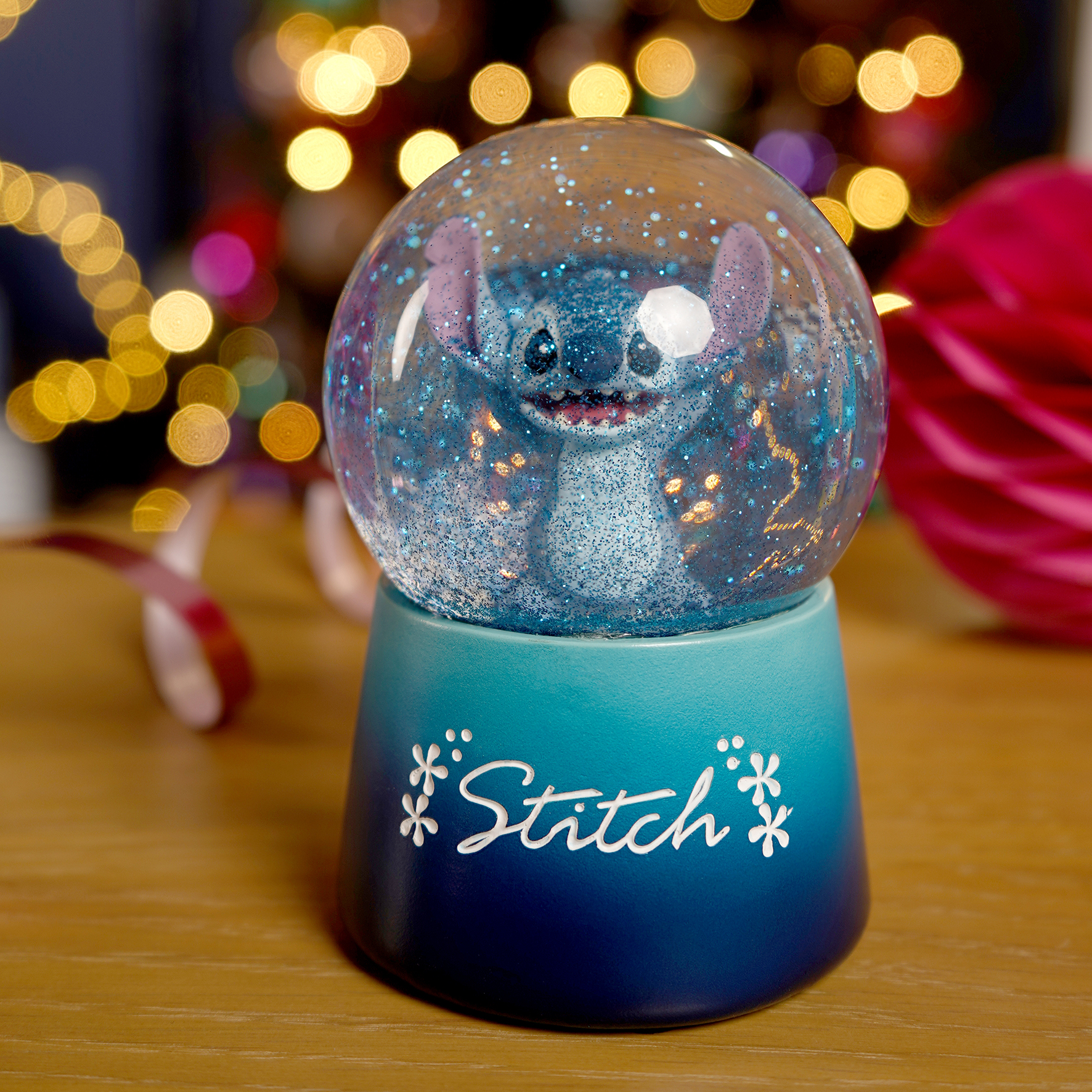 Ein Stitch-Schneeball mit Glitzer auf einem blauen Sockel vor Lichtern.