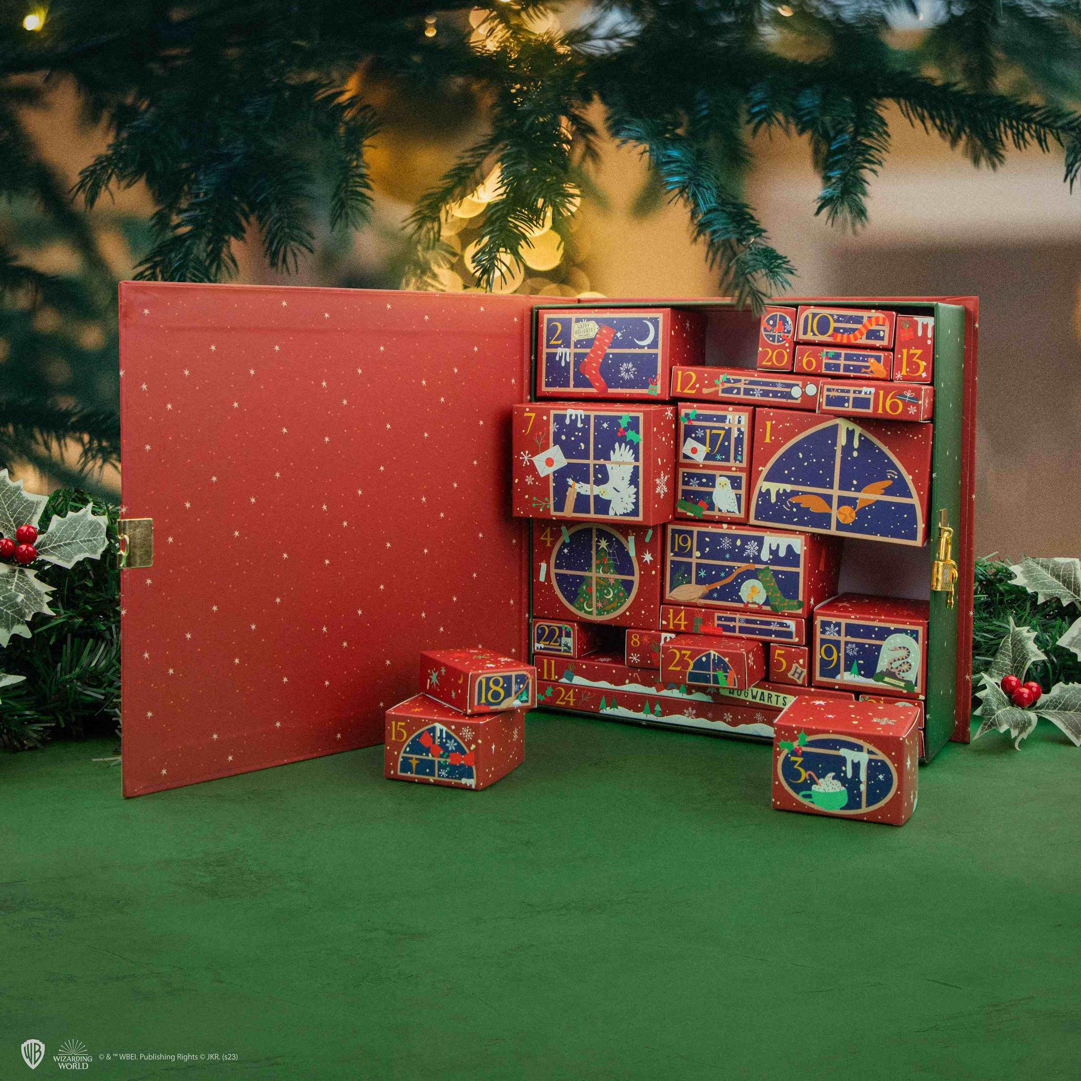Ein aufklappbarer Adventskalender mit nummerierten Schachteln vor einem Weihnachtsbaum.