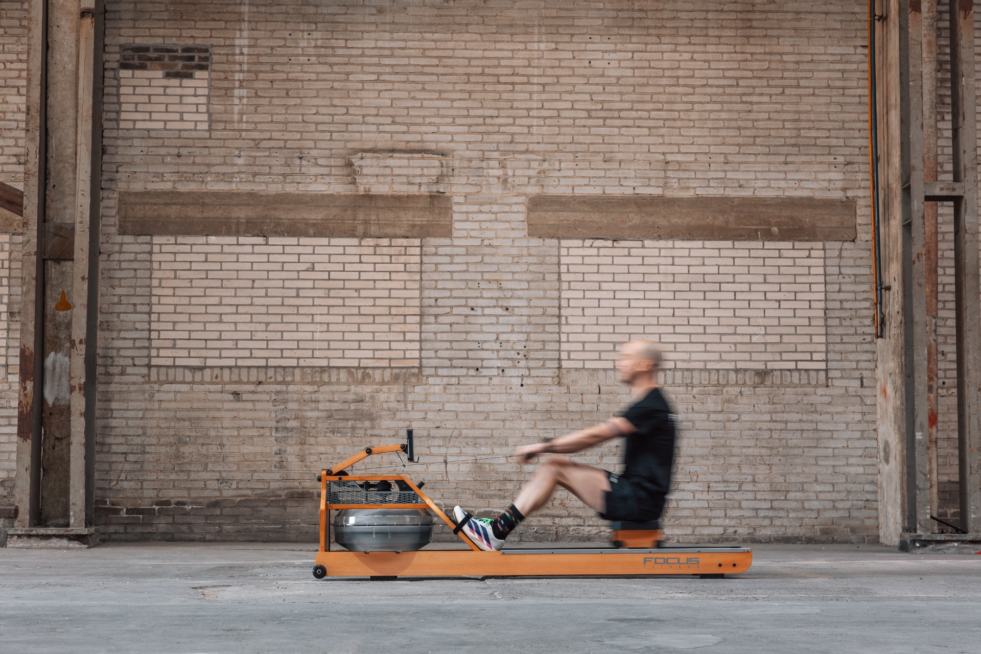 Man rowing on an orange machine in a brick building.