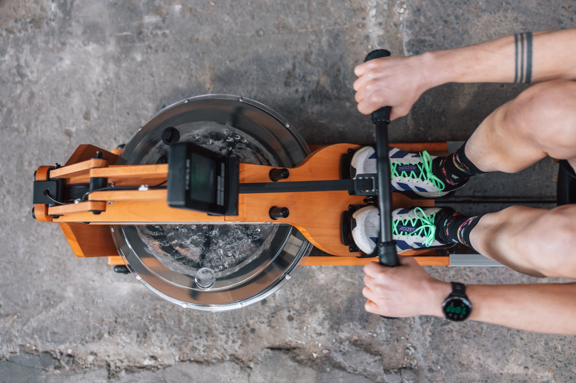 A person on a wooden rowing machine with a water tank and monitor.