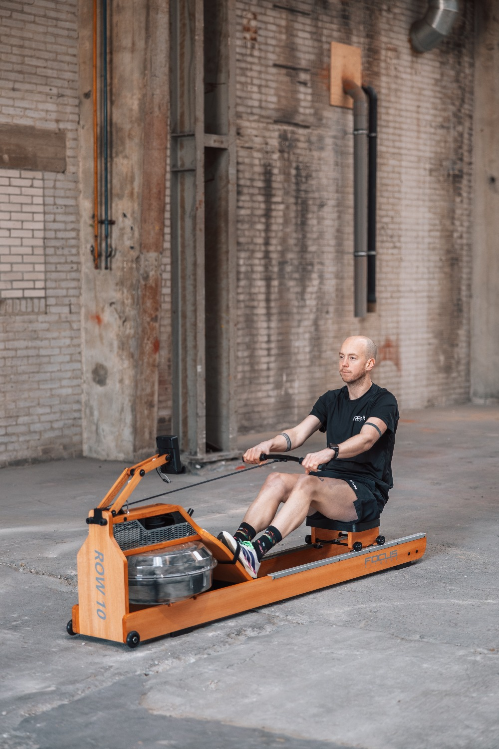 A man works out on an orange rowing machine in a brick-walled warehouse.